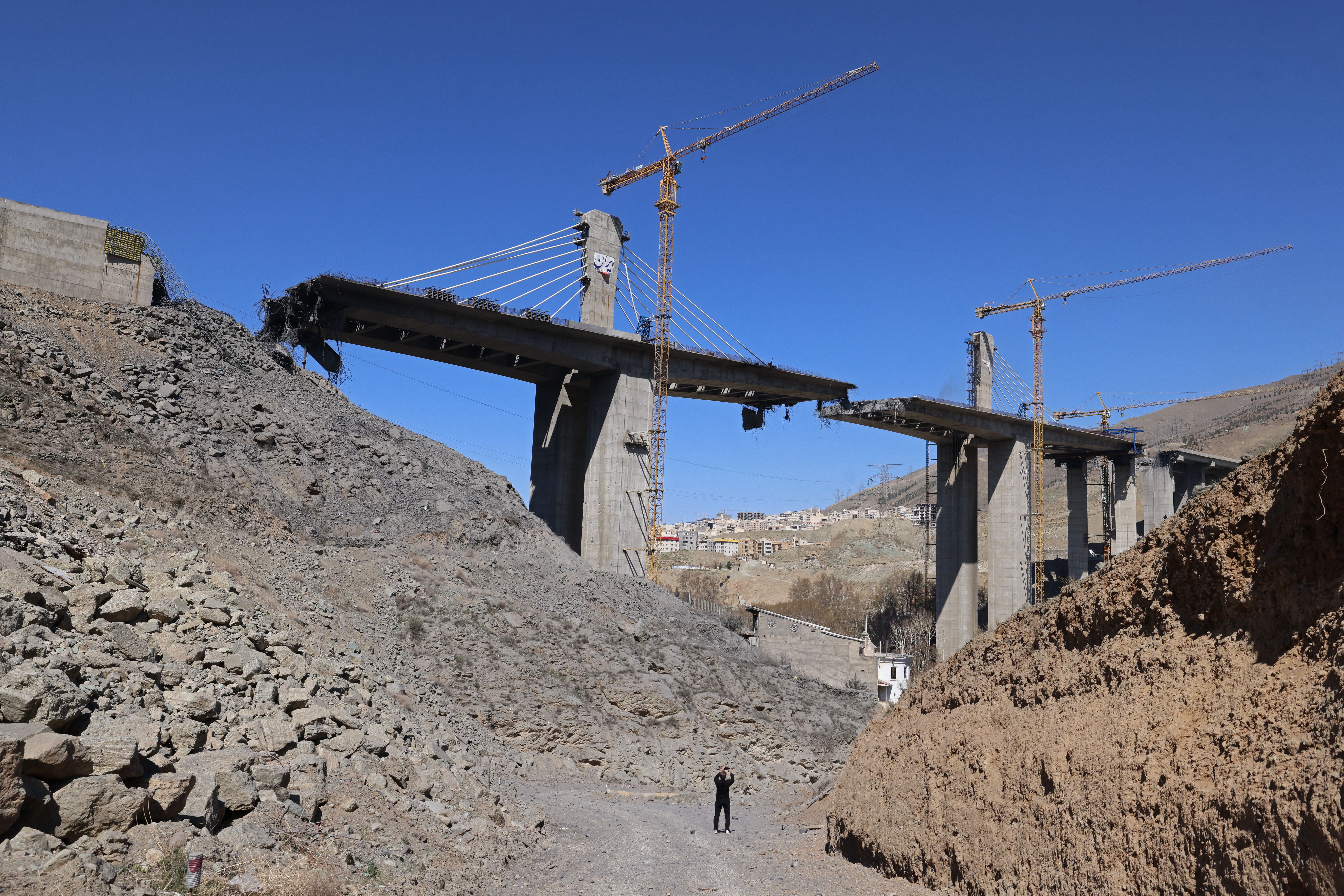  man takes pictures with his mobile phone of the B1 bridge, a day after it was destroyed by a strike in Karaj, around 20miles (35kms) southwest of Tehran, April 3, 2026. US President Donald Trump said on April 2 the tallest bridge in Iran had been destroyed, hours after threatening to bomb the count