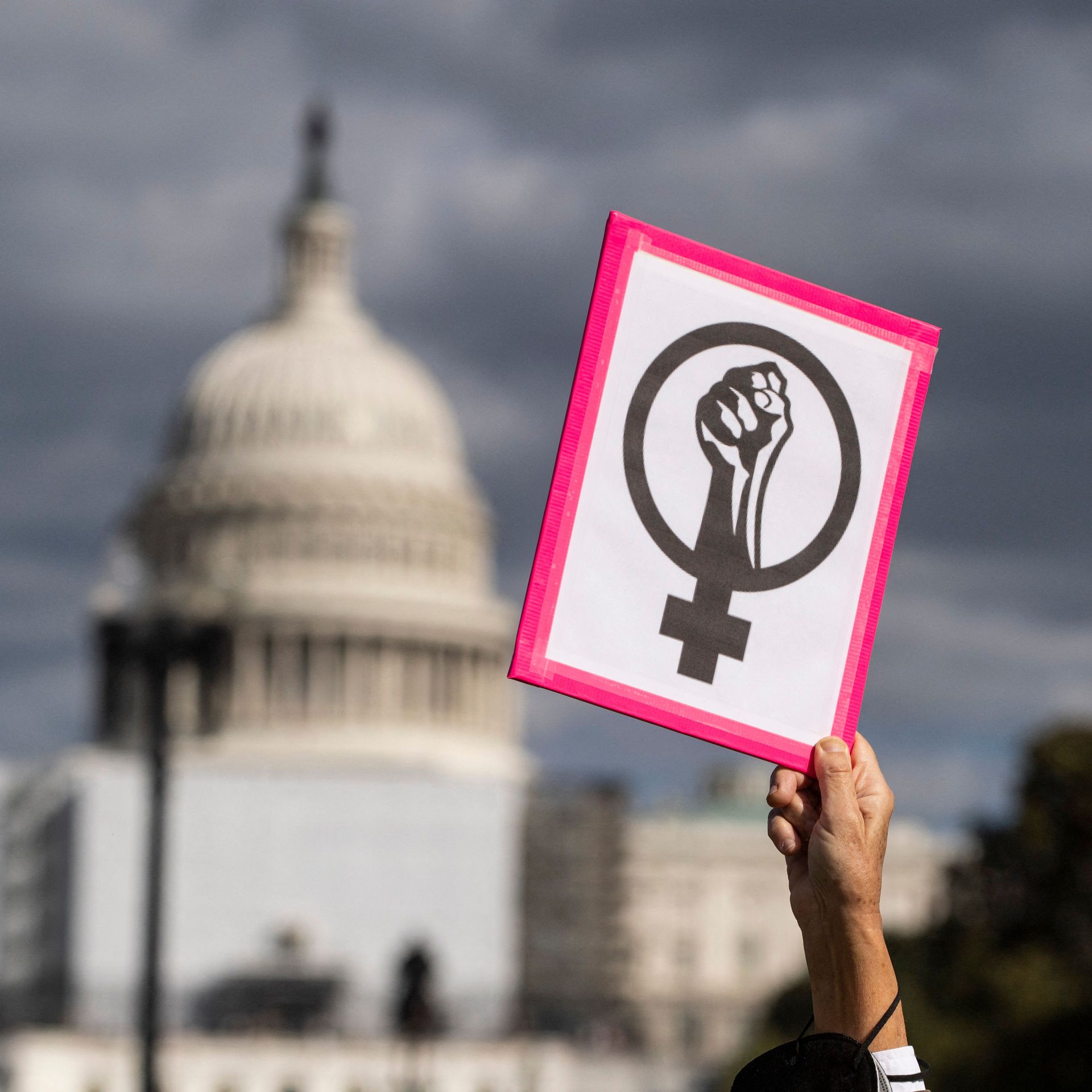 Photo of a hand raising an abortion rights sign against the backdrop of the U.S. Capitol