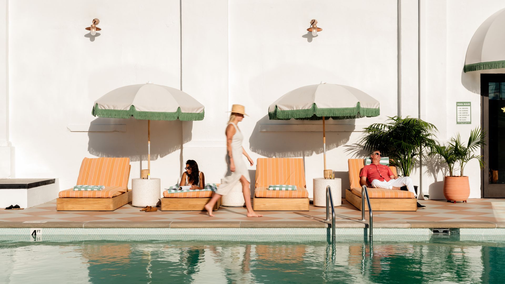 A woman walks past loungers next to a pool.