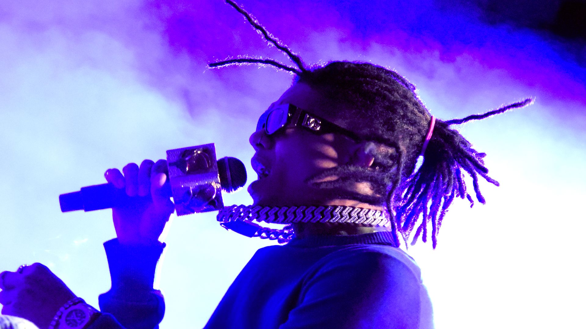 A rapper in sunglasses sings into a microphone bathed in purple light