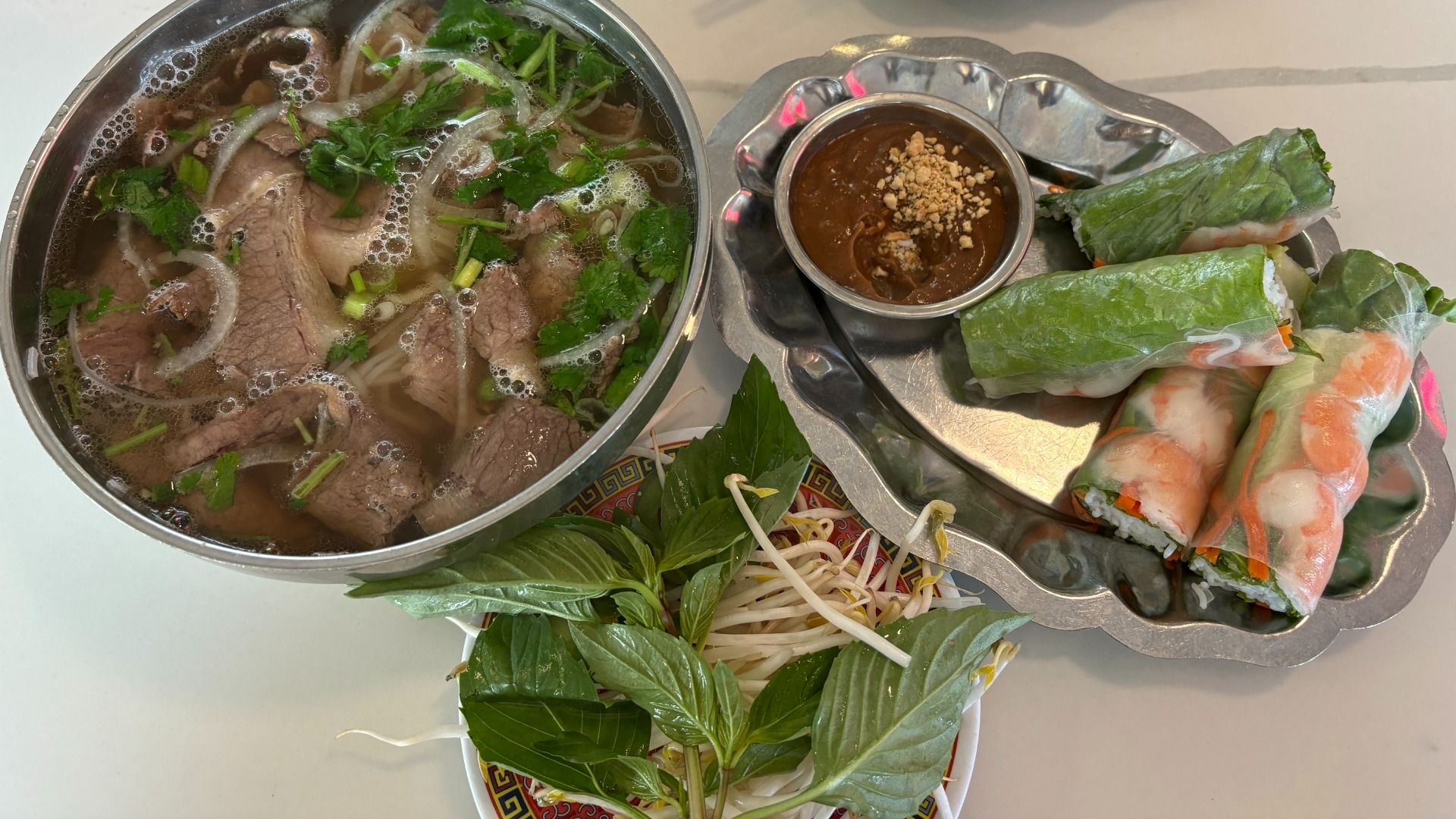 Pho, spring rolls, and fresh garnishes on a restaurant table. 