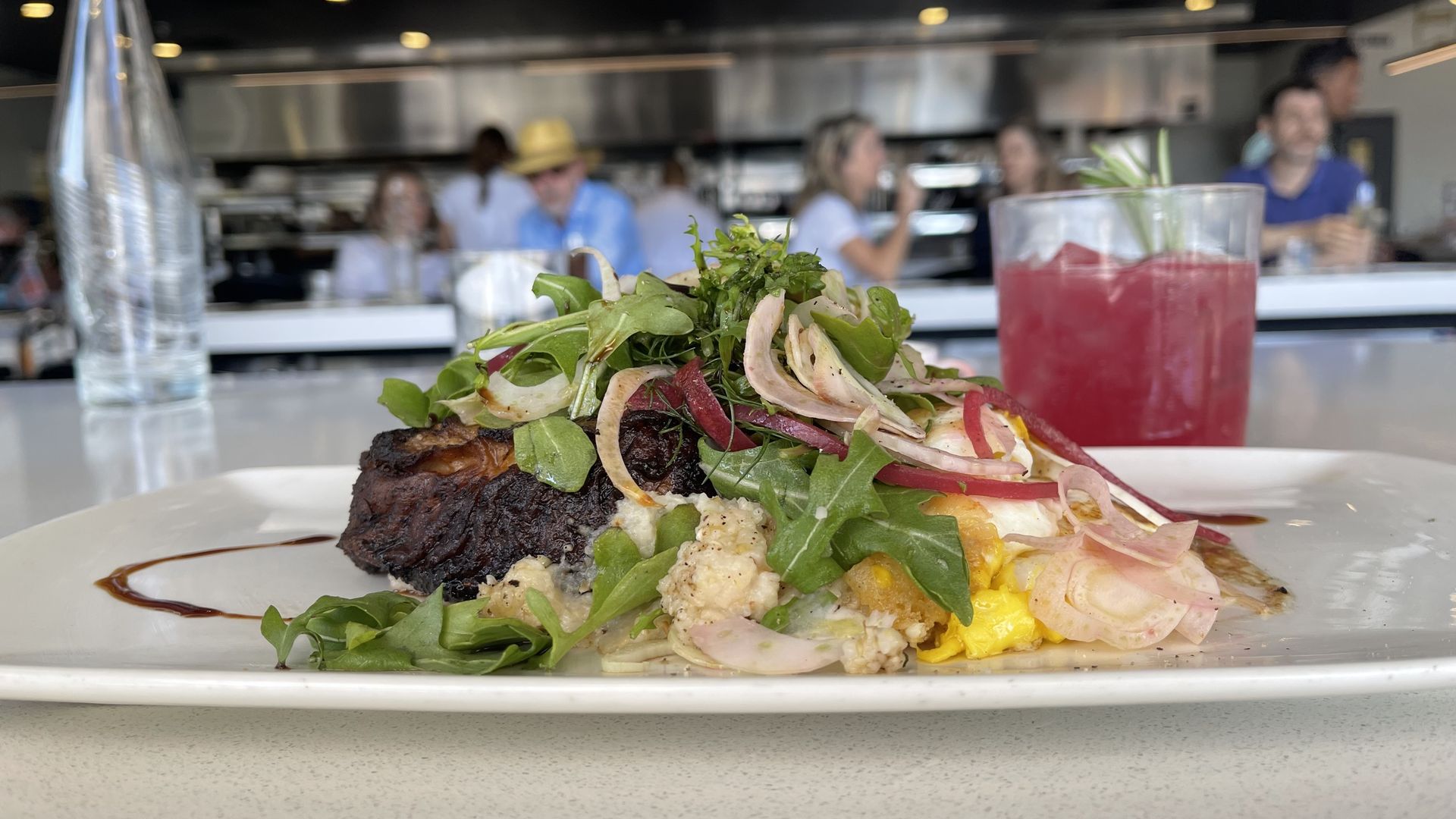 a plate of food and a cocktail in front of people eating at a counter