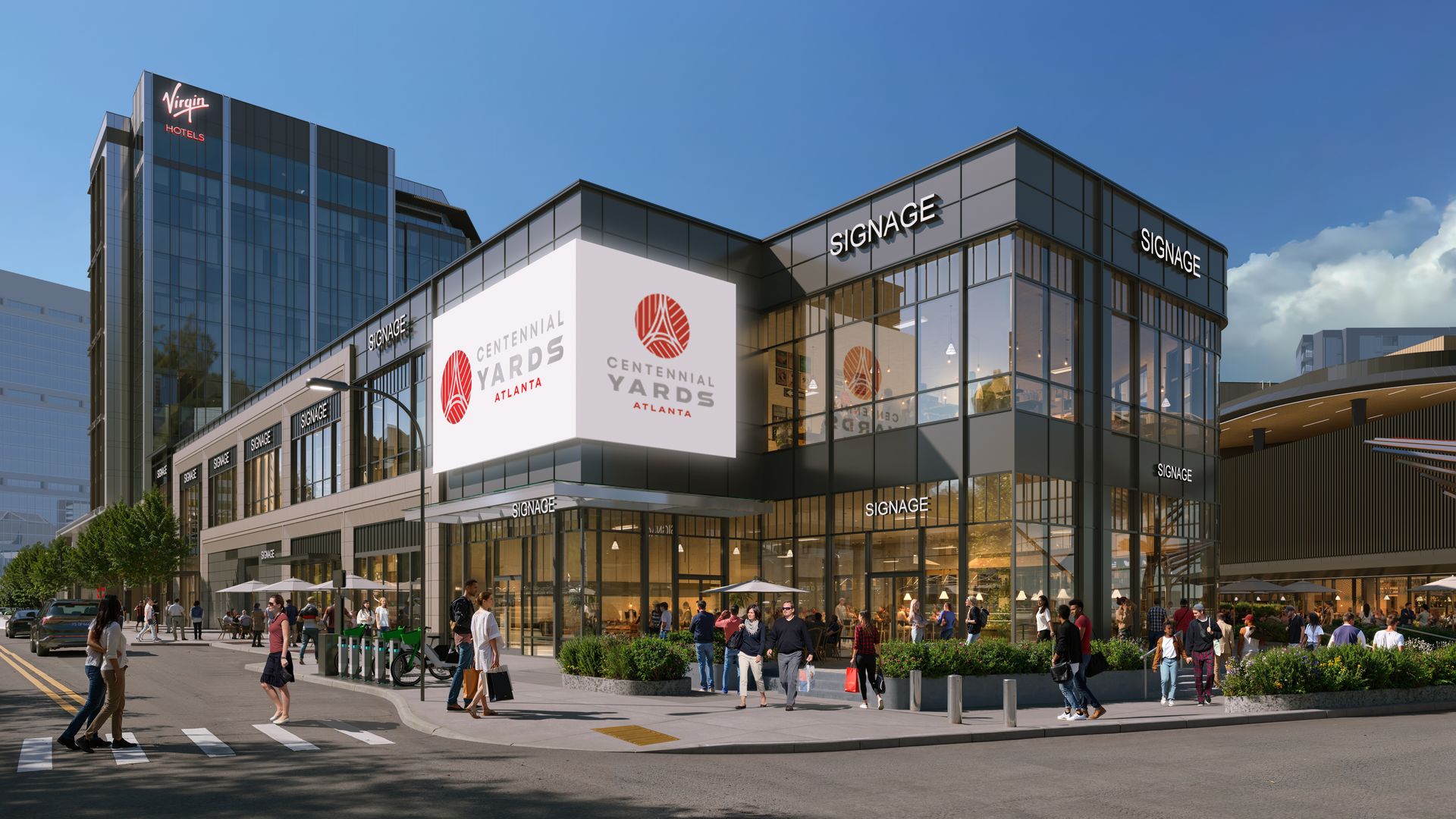Modern glass-front complex with a white panel reading "CENTENNIAL YARDS ATLANTA" and a tall blue tower with a red "Virgin Hotels" sign. Pedestrians stroll the plaza under a clear blue sky.