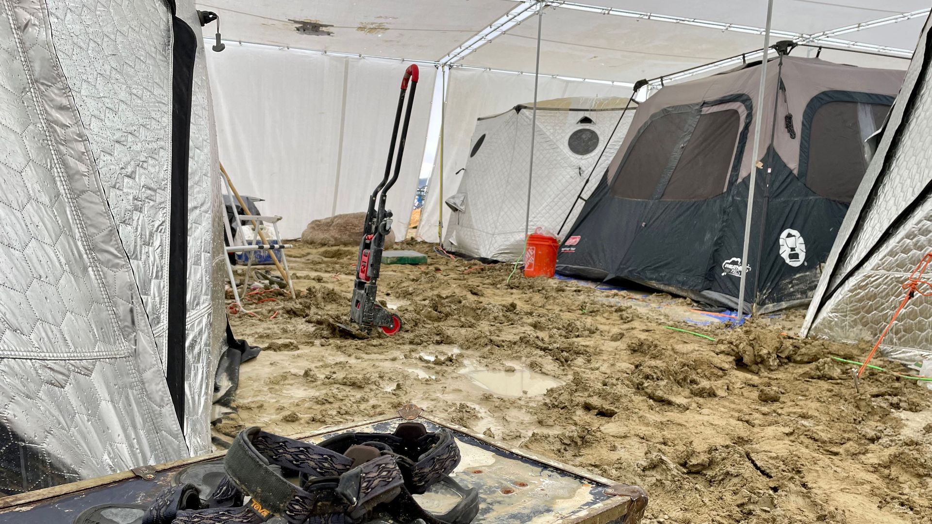A pair of Teva sandals are seen on a chest in the middle of tents sitting in a muddy desert plain on September 3, 2023, after heavy rains turned the annual Burning Man festival site in Nevada's Black Rock desert into a mud pit.