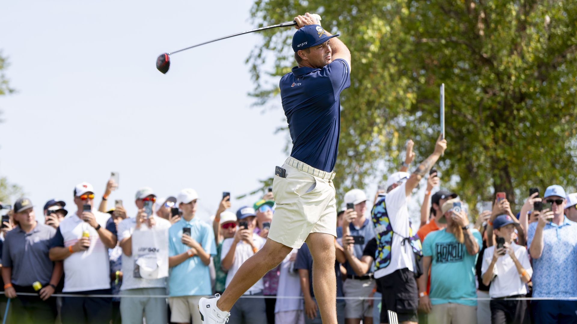 A golfer swings his club with a crowd behind him