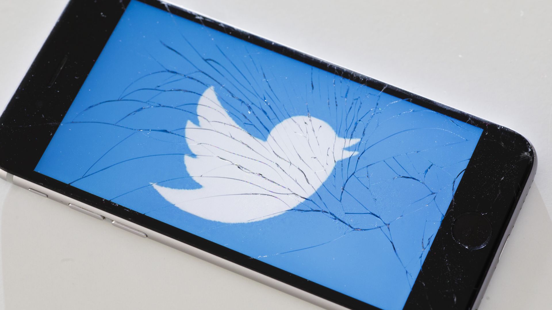 A Twitter logo appears on an iPhone with a cracked screen.