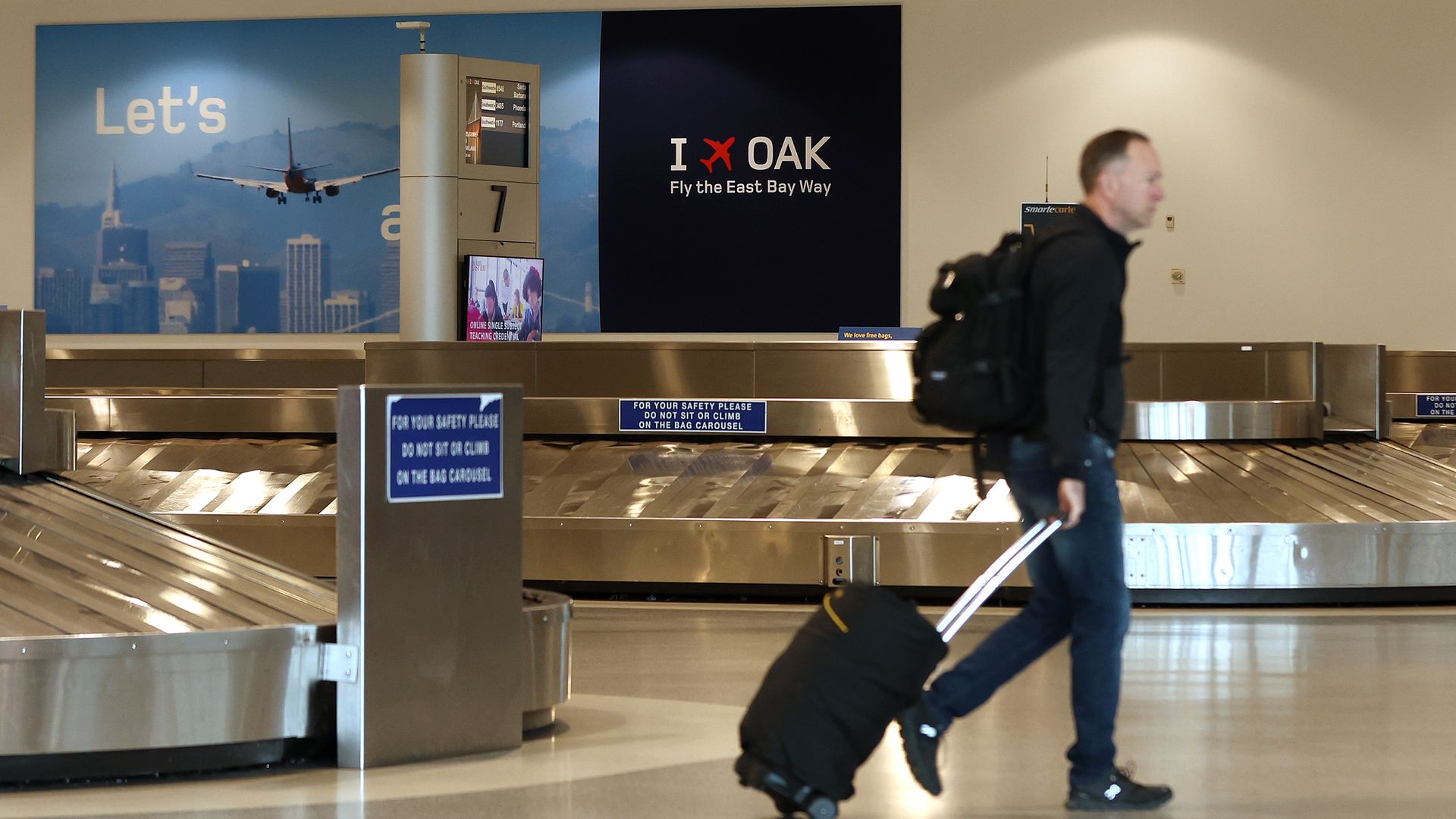 Photo of a passenger with a suitcase walking around the baggage claim area in Oakland's airport