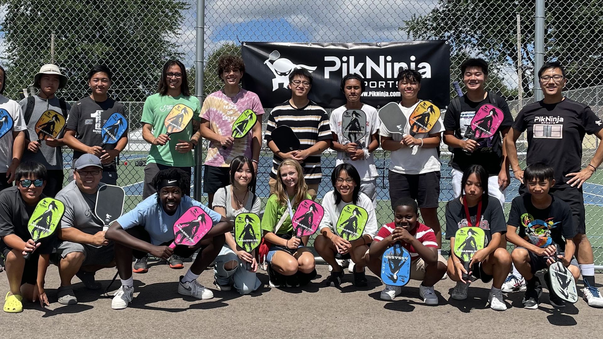 a group of young people in athletic clothes holding bright green pink and blue paddle balls in front of a court