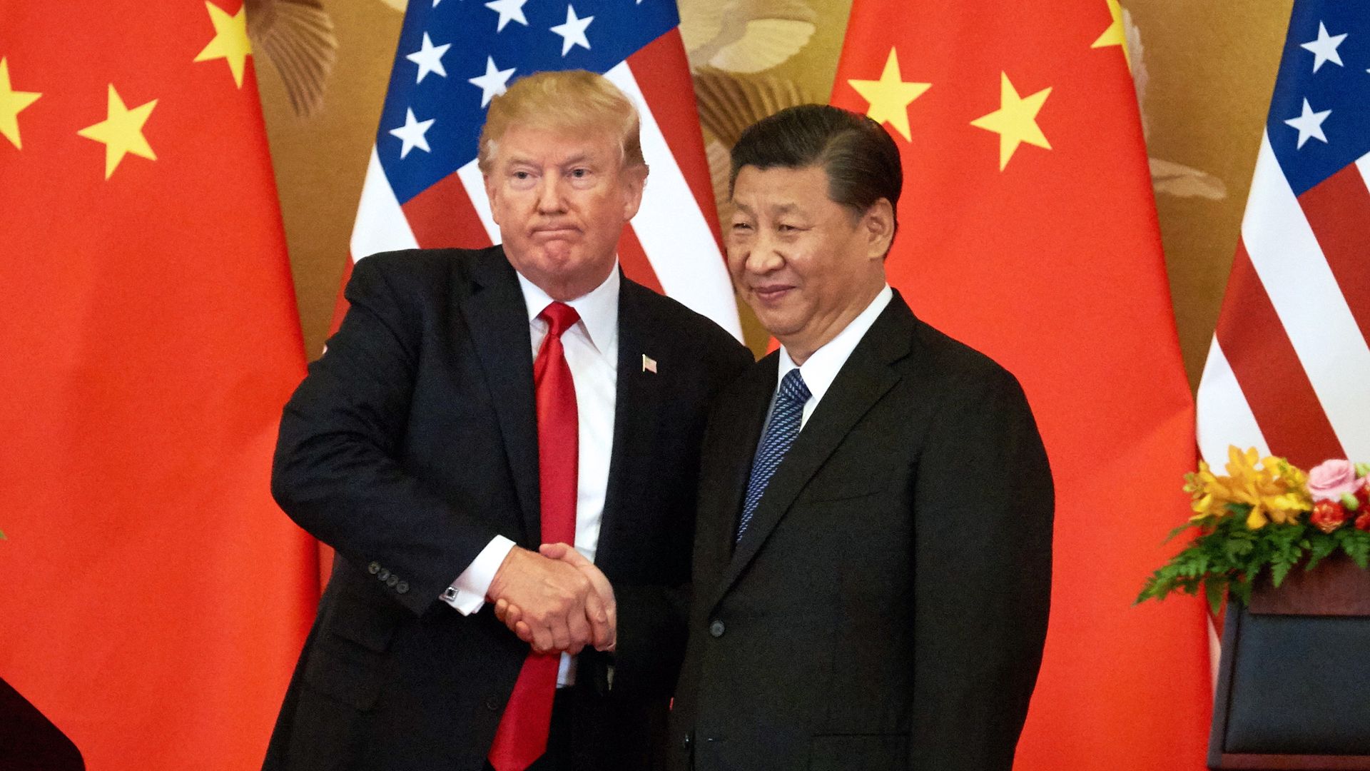 President Trump and Xi Jingping shake hands in front of flags from their respective countries 
