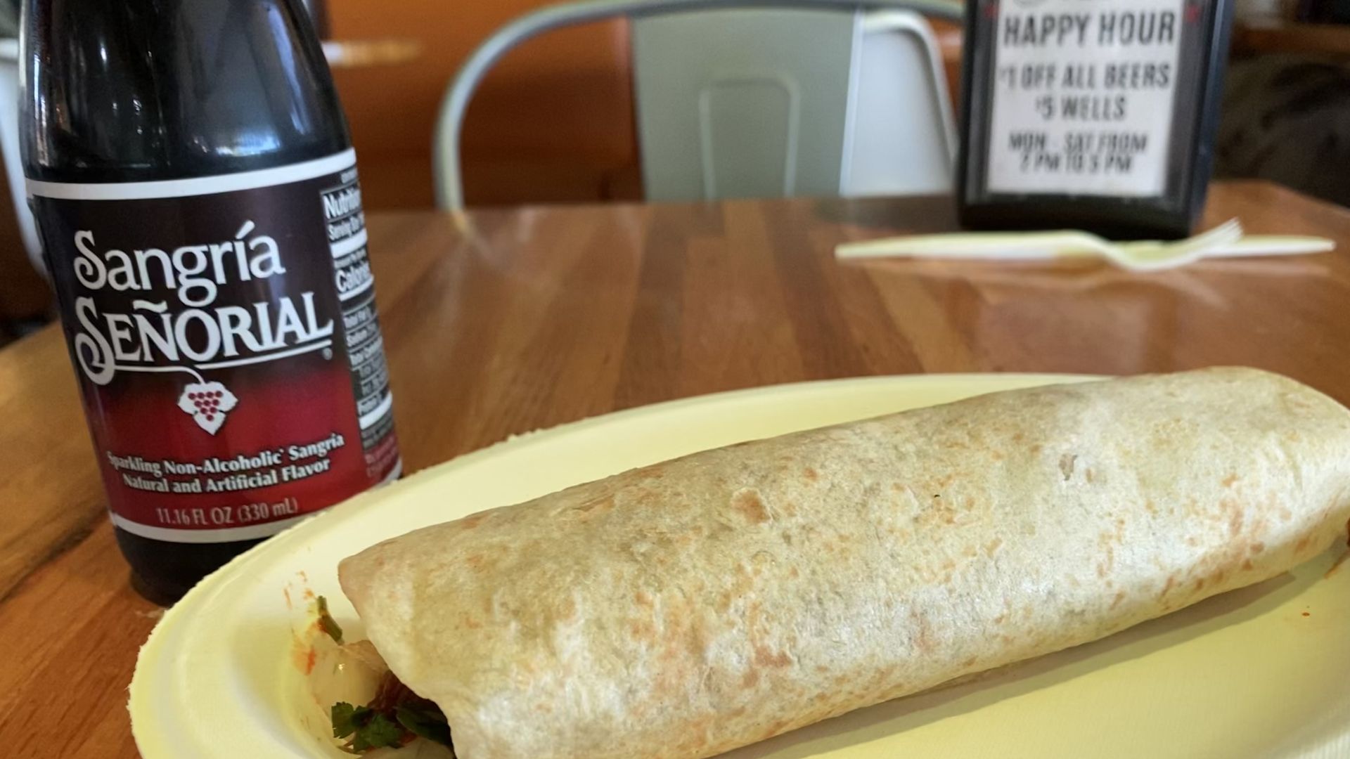 A burrito on a paper plate with shredded beef coming out of the end next to a glass soft drink bottle.