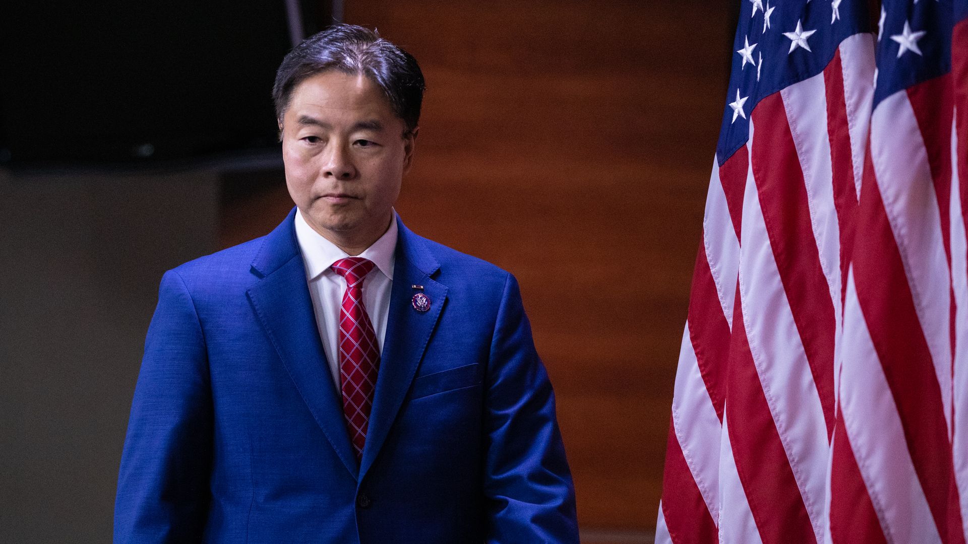 A person in a blue suit and red tie walks by a U.S. flag