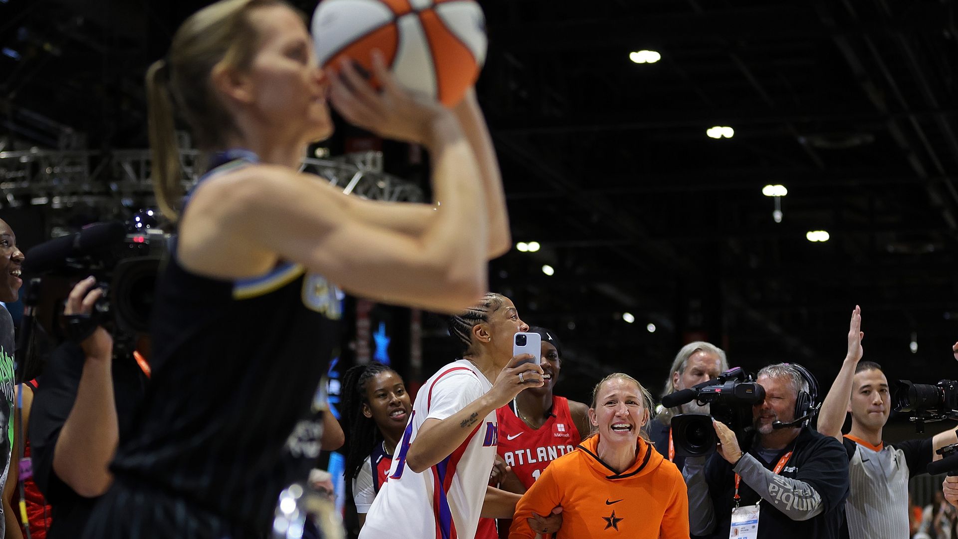 Photo of fans cheering on a woman shooting a basketball. 