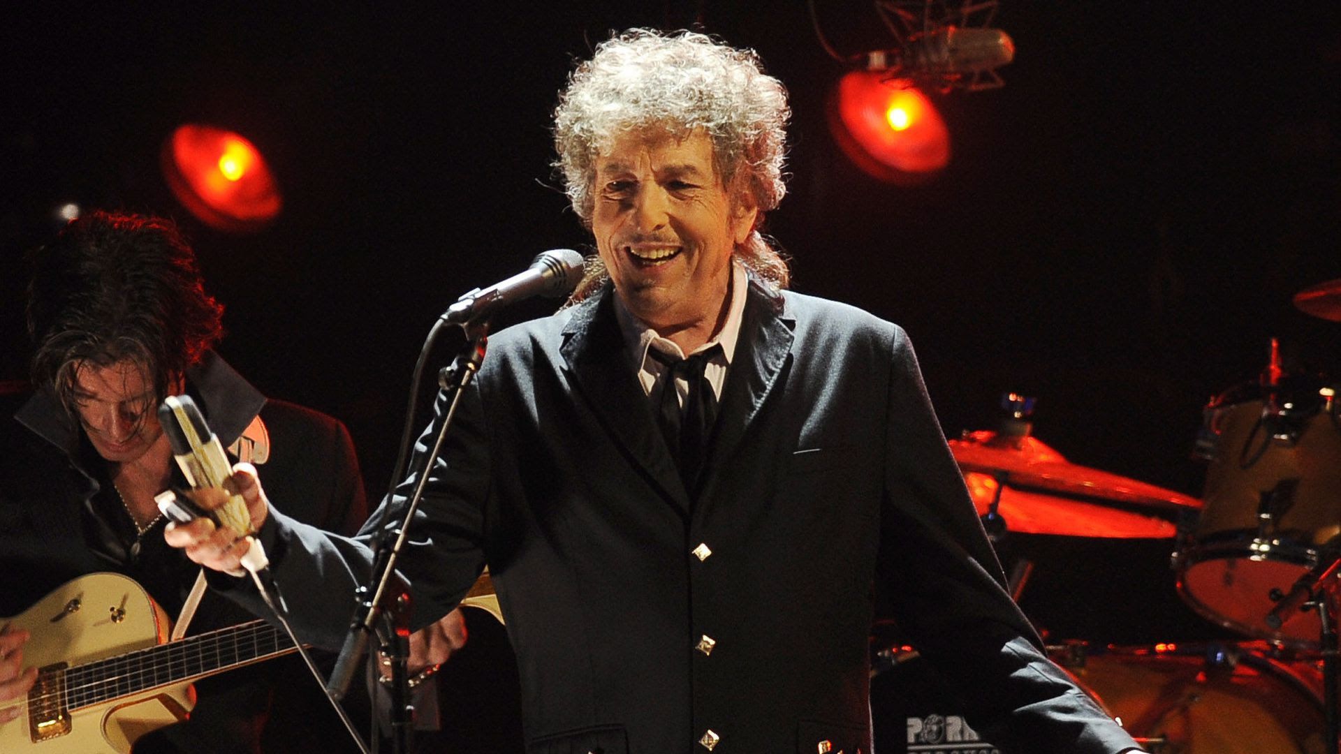 Bob Dylan on stage grinning and holding a microphone