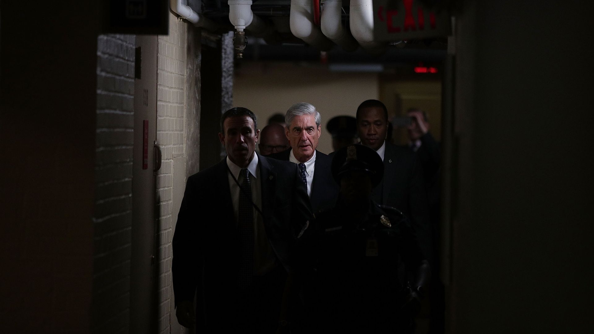 Robert Mueller walks with a group of people through a dark hallway.
