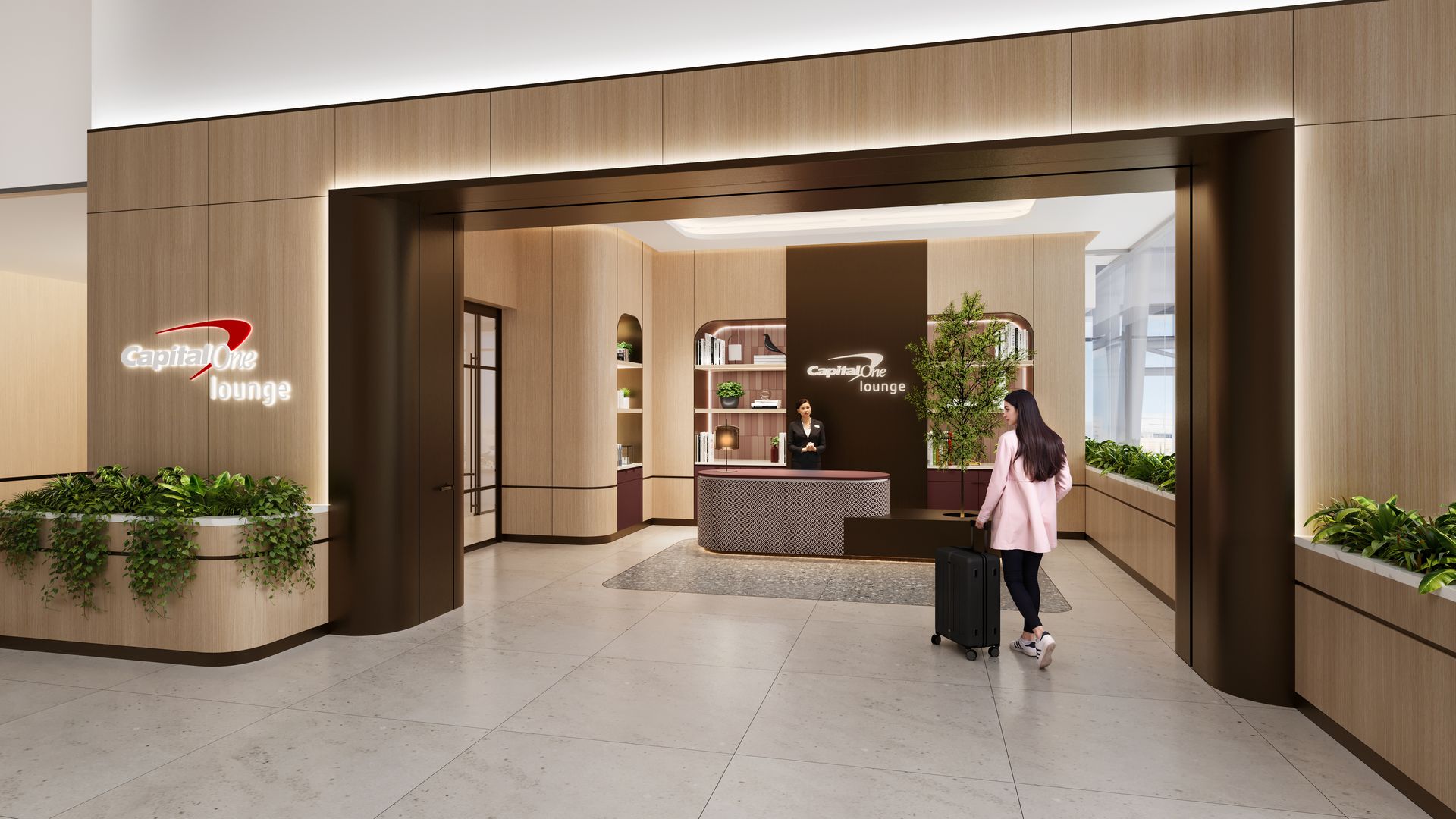 Entrance to Capital One lounge with light wood walls, plants, and illuminated signs. A woman in a pink coat pulls a black suitcase toward a reception desk with an attendant.
