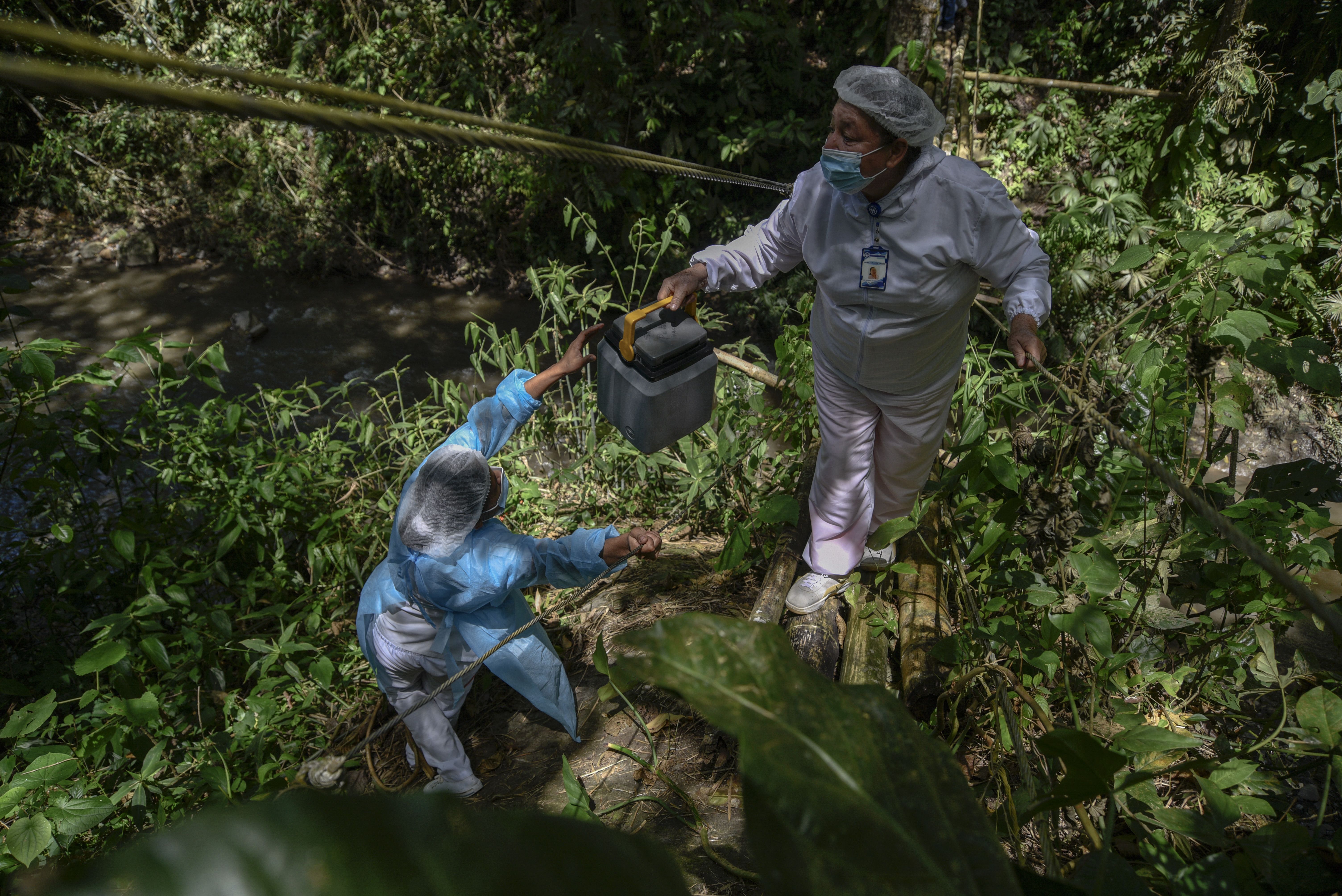 Health care workers cross a cane bridge in Colombia to administer a COVID vaccine to a rural resident.