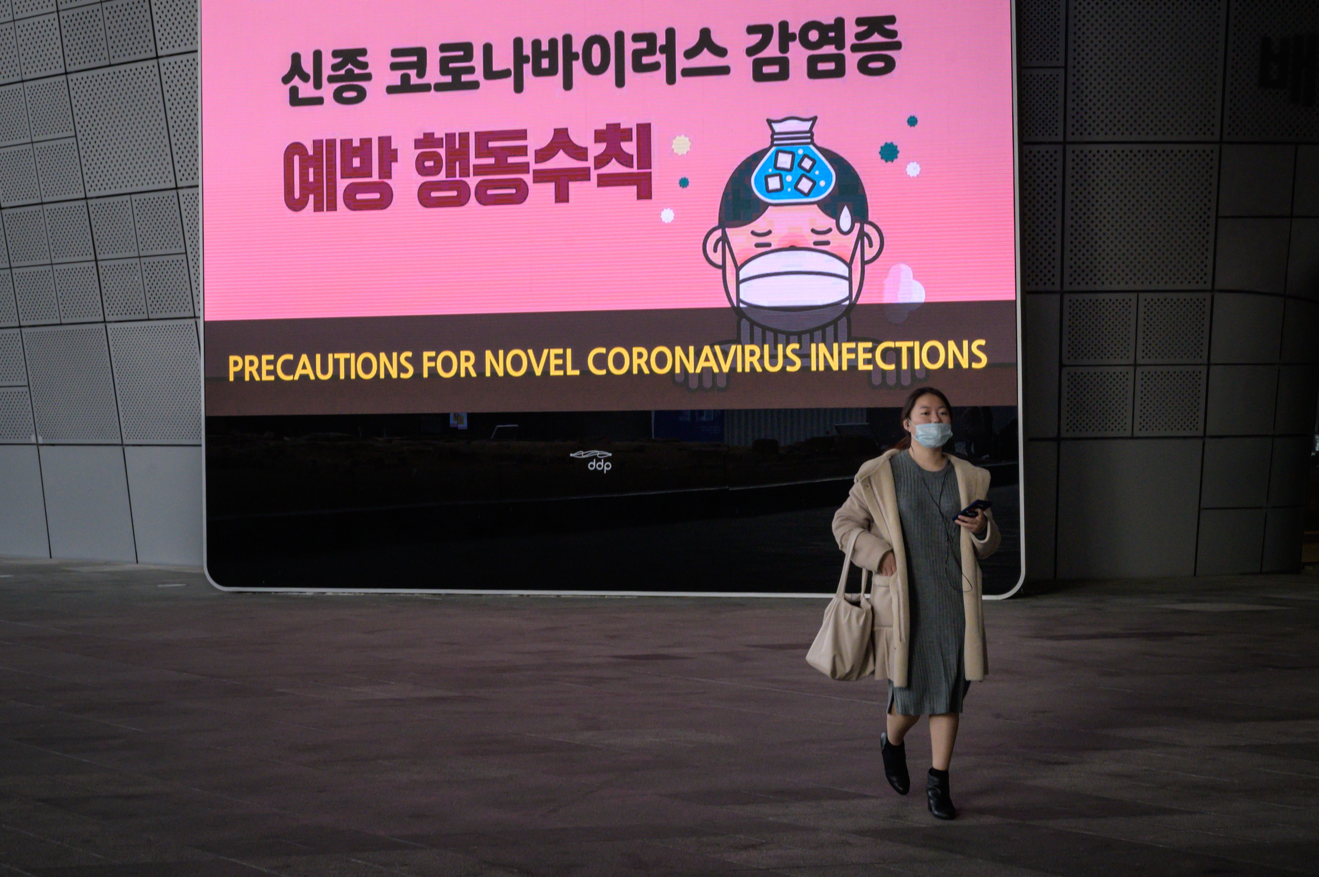 A woman wearing a face mask walks before a screen displaying preventative measures against the novel coronavirus, at Dongdaemun Design Plaza in Seoul. 