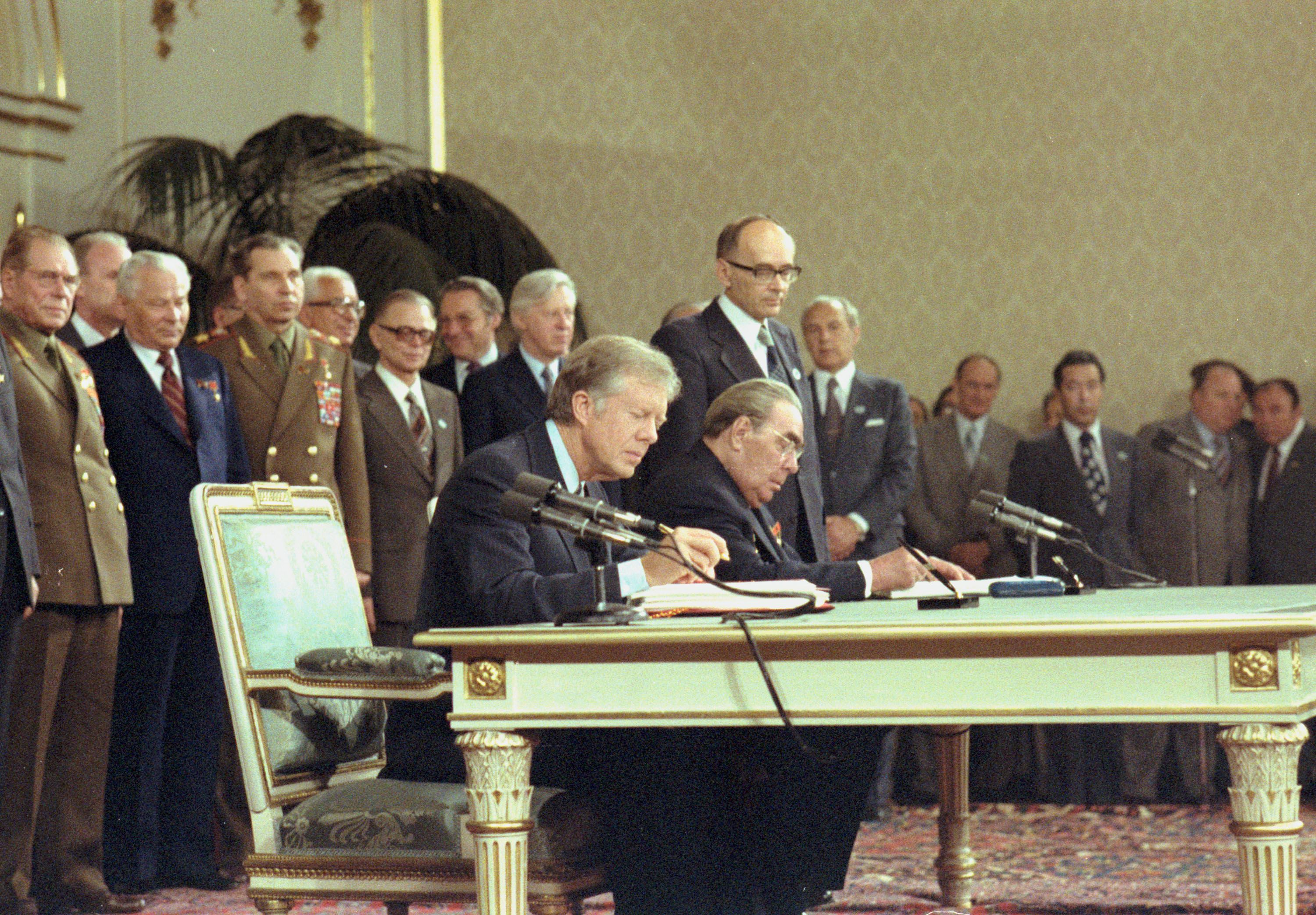 Jimmy Carter in the final years of his presidency, signing a treaty alongside the Soviet Leader, with military and other dignitaries surrounding them