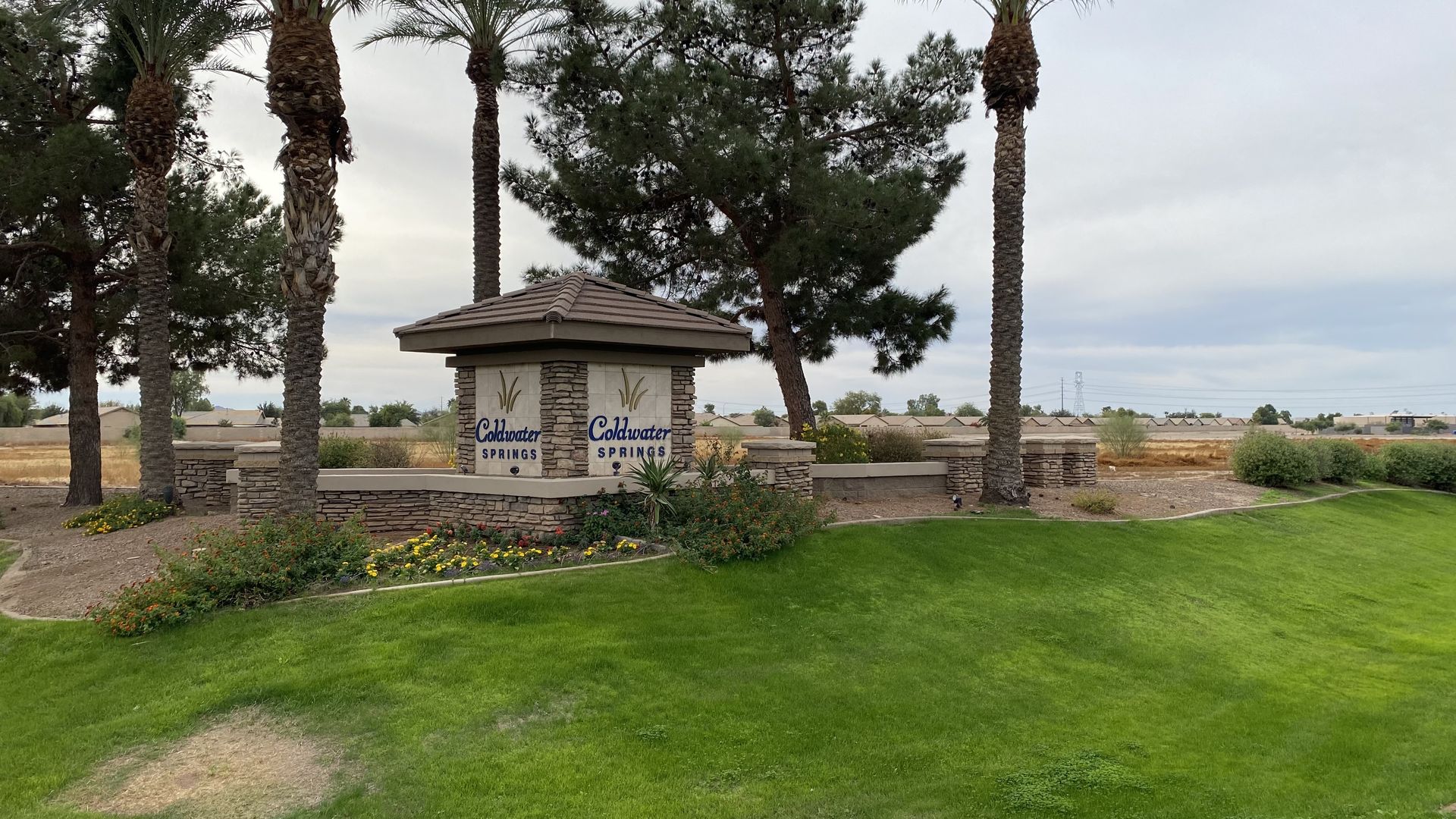 A decorative pillar that reads Coldwater Springs with a large vacant dirt lot behind it. 