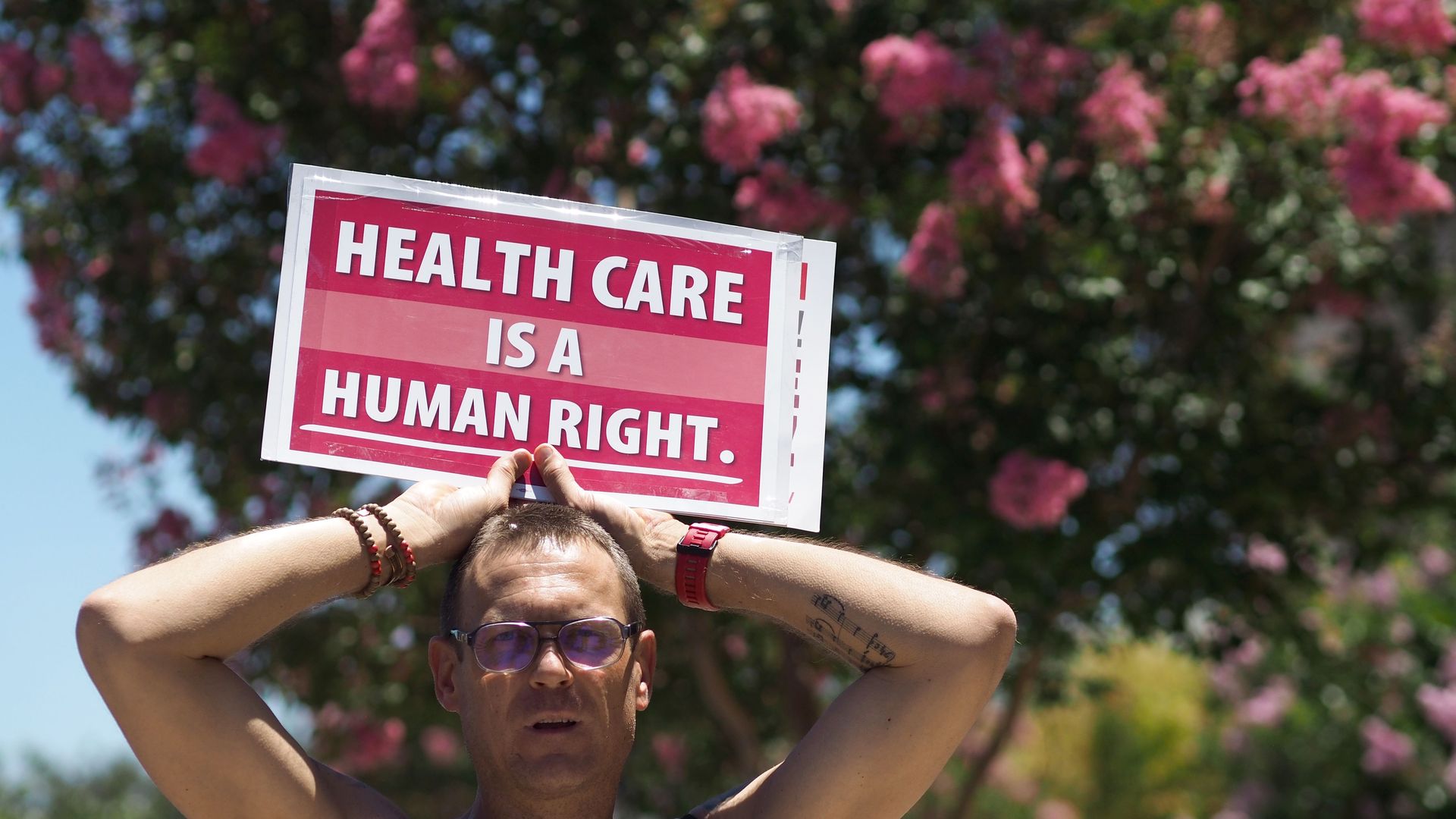 A man holds a sign that reads, "Health care is a human right." 