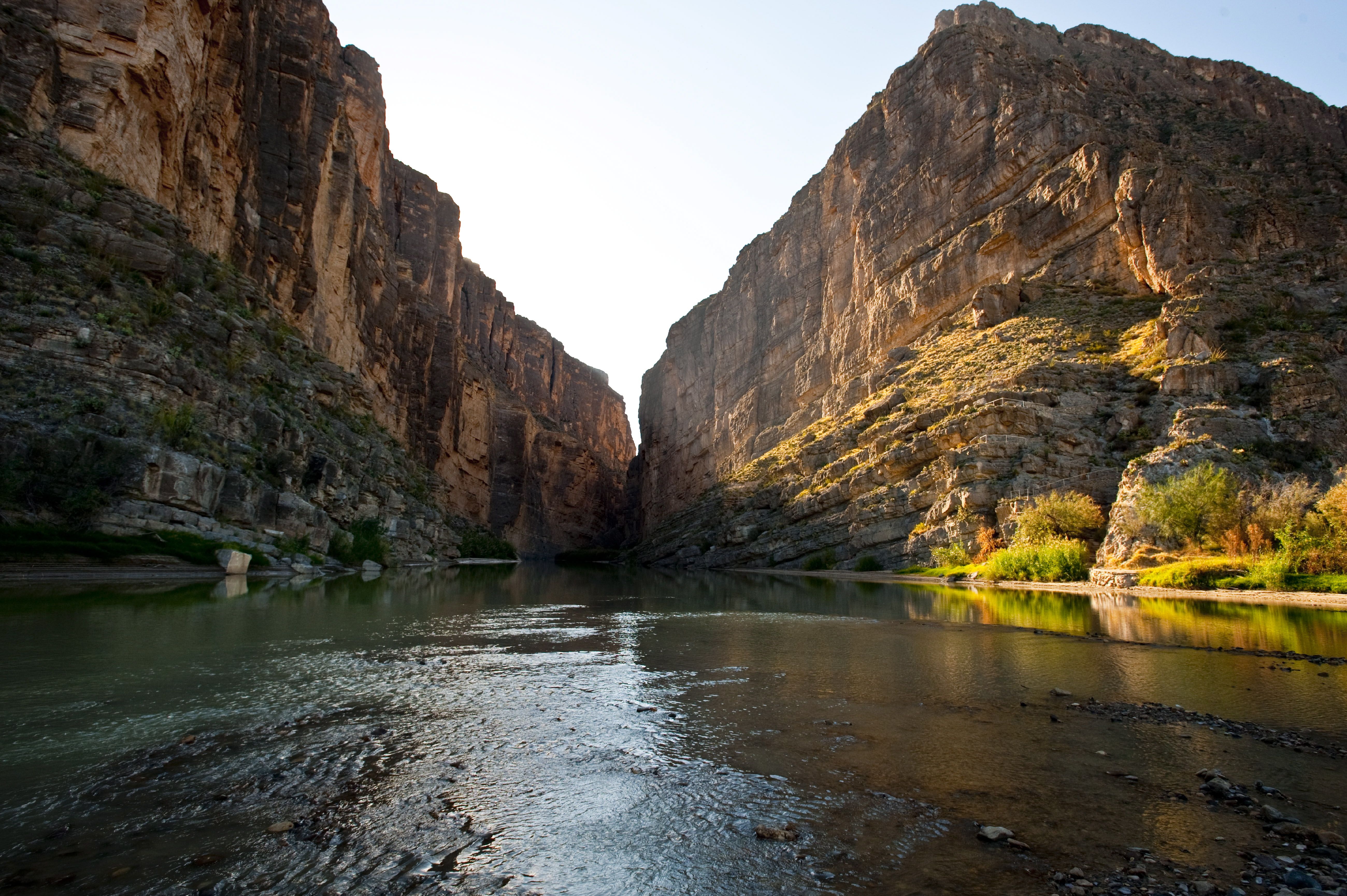Canyon cliffs surround a river lit up with evening sun, with the sky peeking through in the middle