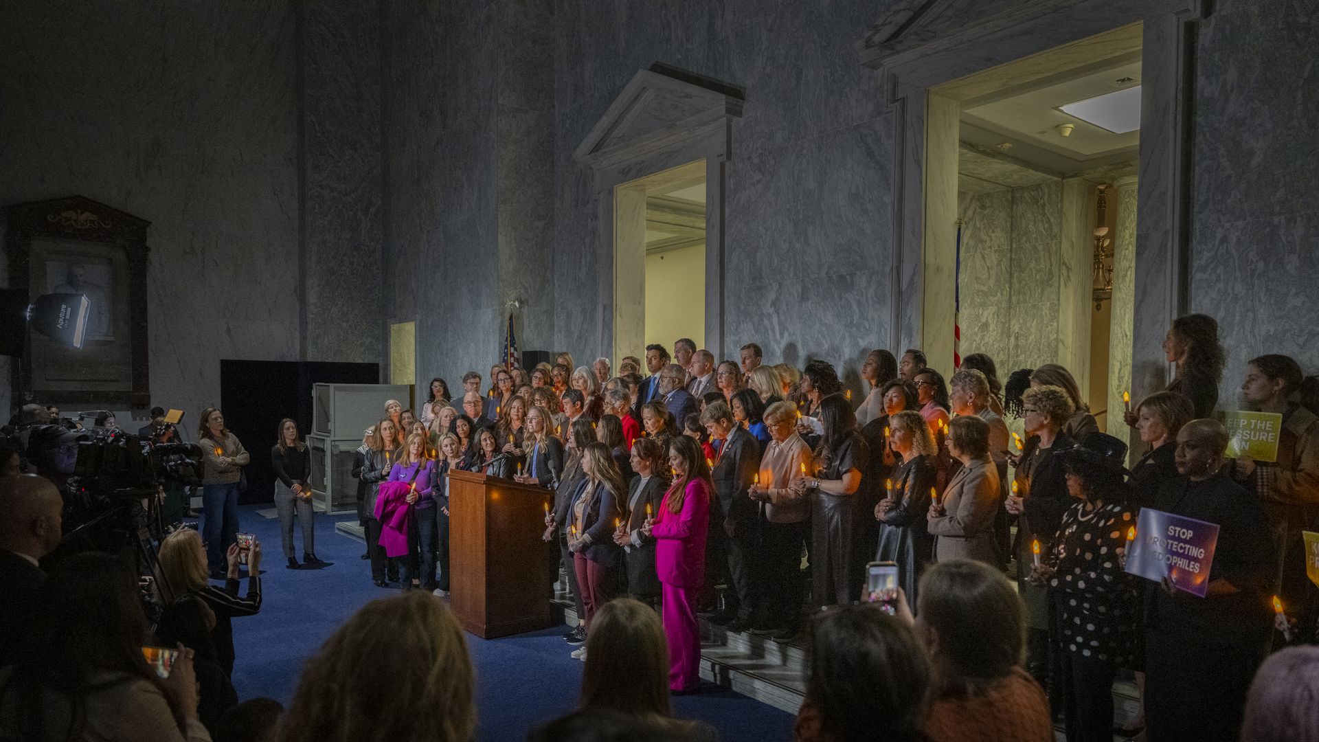 A large group of individuals gathered around a podium holding small candles