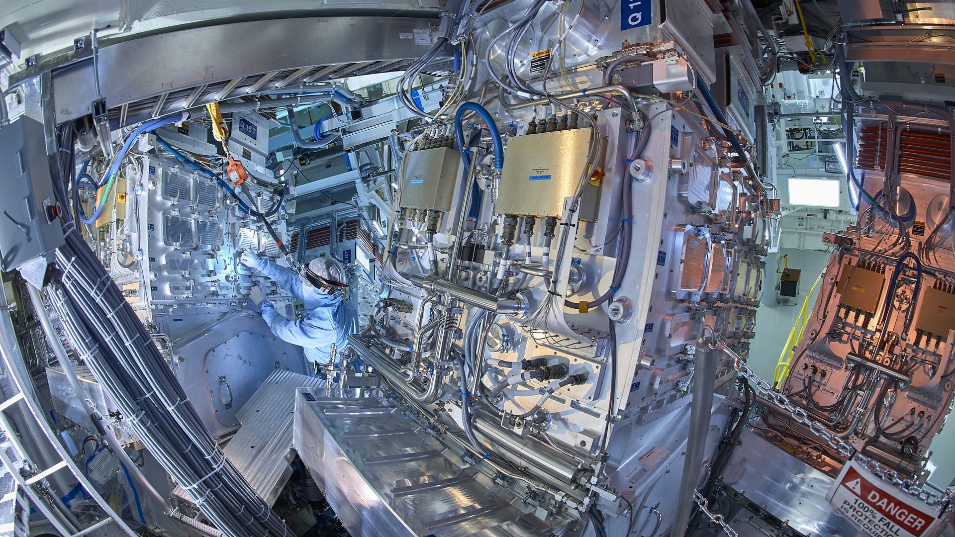 Photo of a person checking wires and tubes in a laser facility 