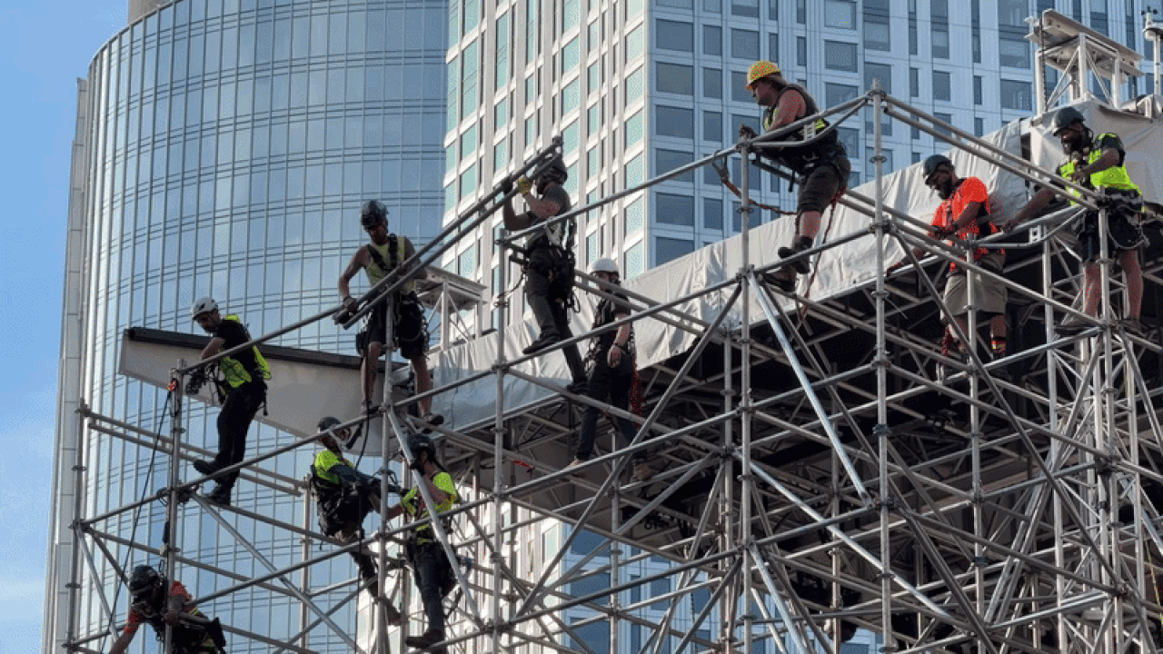 Workers stand on poles dozens of feet high constructing the 2026 FIFA World Cup Fan Fest zone outside City Hall on Tuesday, May 26, 2026.