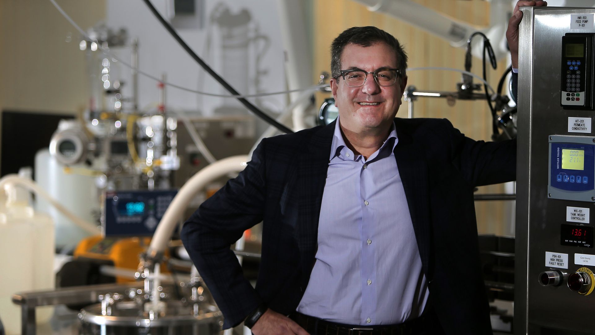 Alnylam CEO Dr. John Maraganore poses for a portrait with lab equipment behind.
