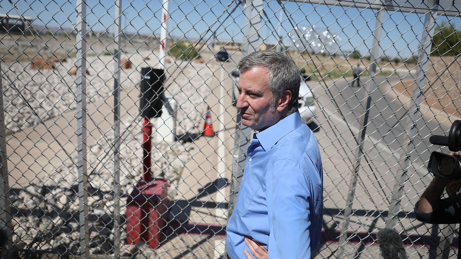 Mayor Bill de Blasio stands by a chain-link fence.