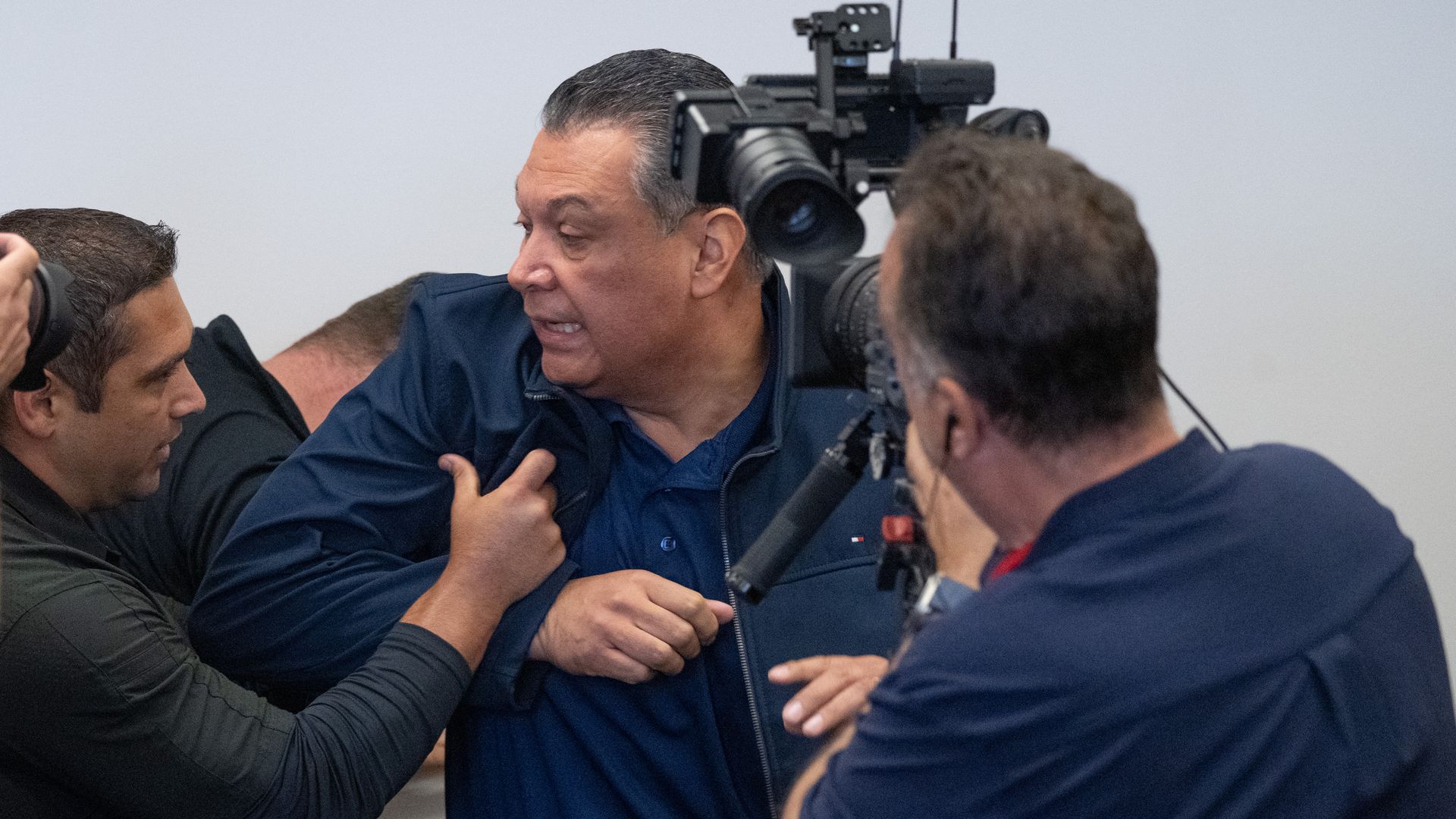 Sen. Alex Padilla is pushed out of a news conference as a photographer films the moment.
