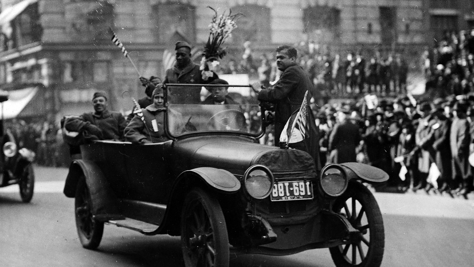 Croix de guerre medal winner Private William Henry Johnson (1892 - 1929) holds a bouquet of flowers and stands in an open top automobile during the victory parade in New York, February 17, 1919. 