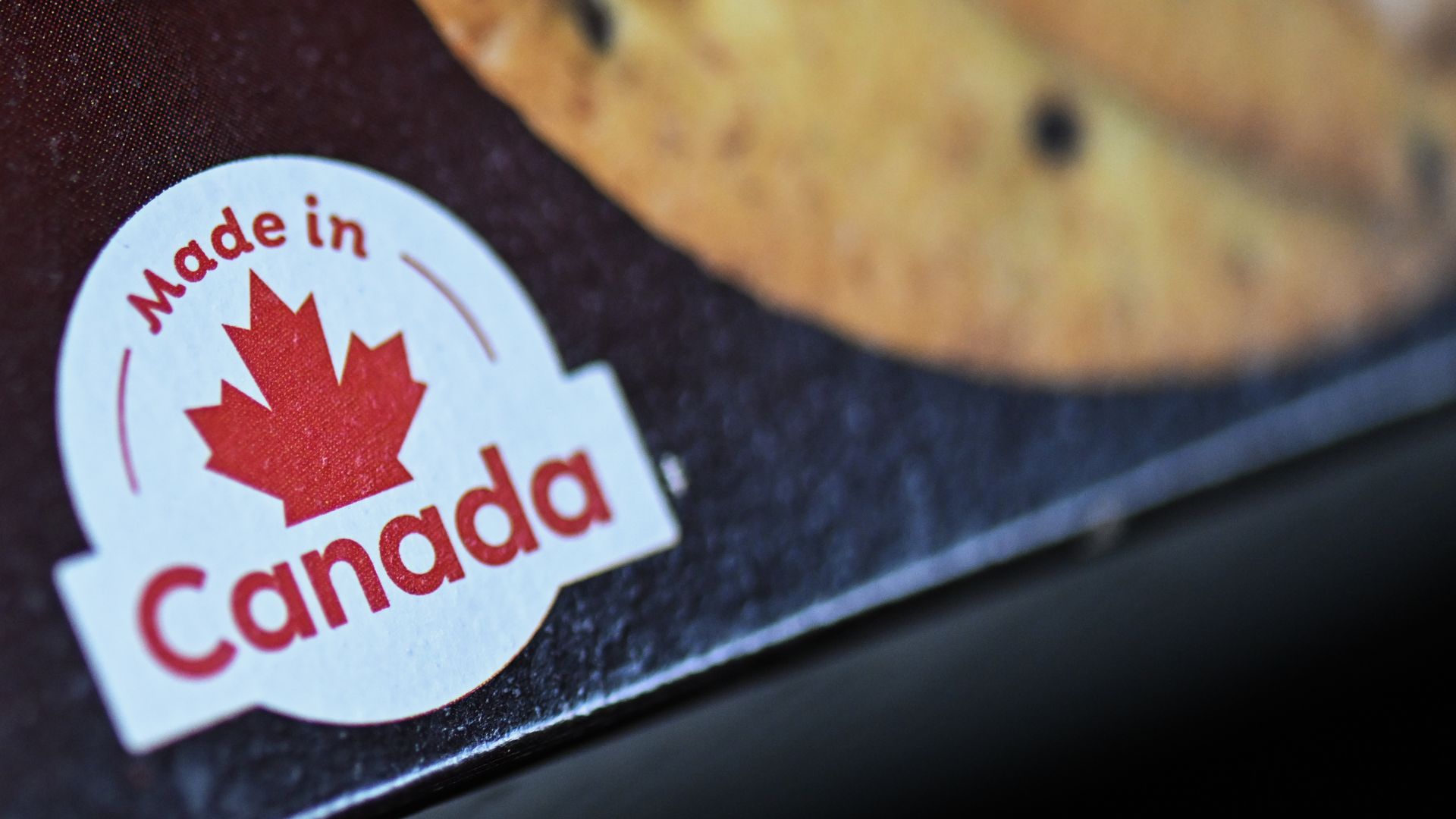Close-up of a white circular sticker with a red maple leaf and the words "Made in Canada" on dark fabric.