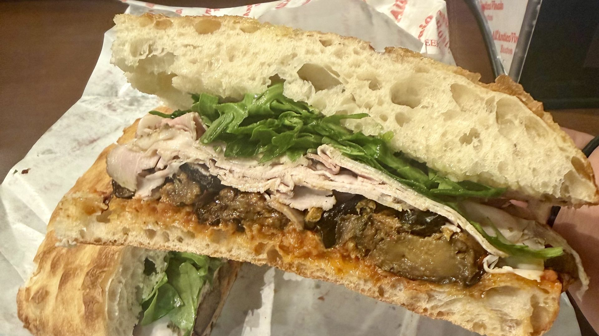 Close-up of L'Inferno, a massive sandwich from All'Antico Vinaio with porchetta, nduja, spicy eggplant, spicy zucchini and  arugula on their bread.