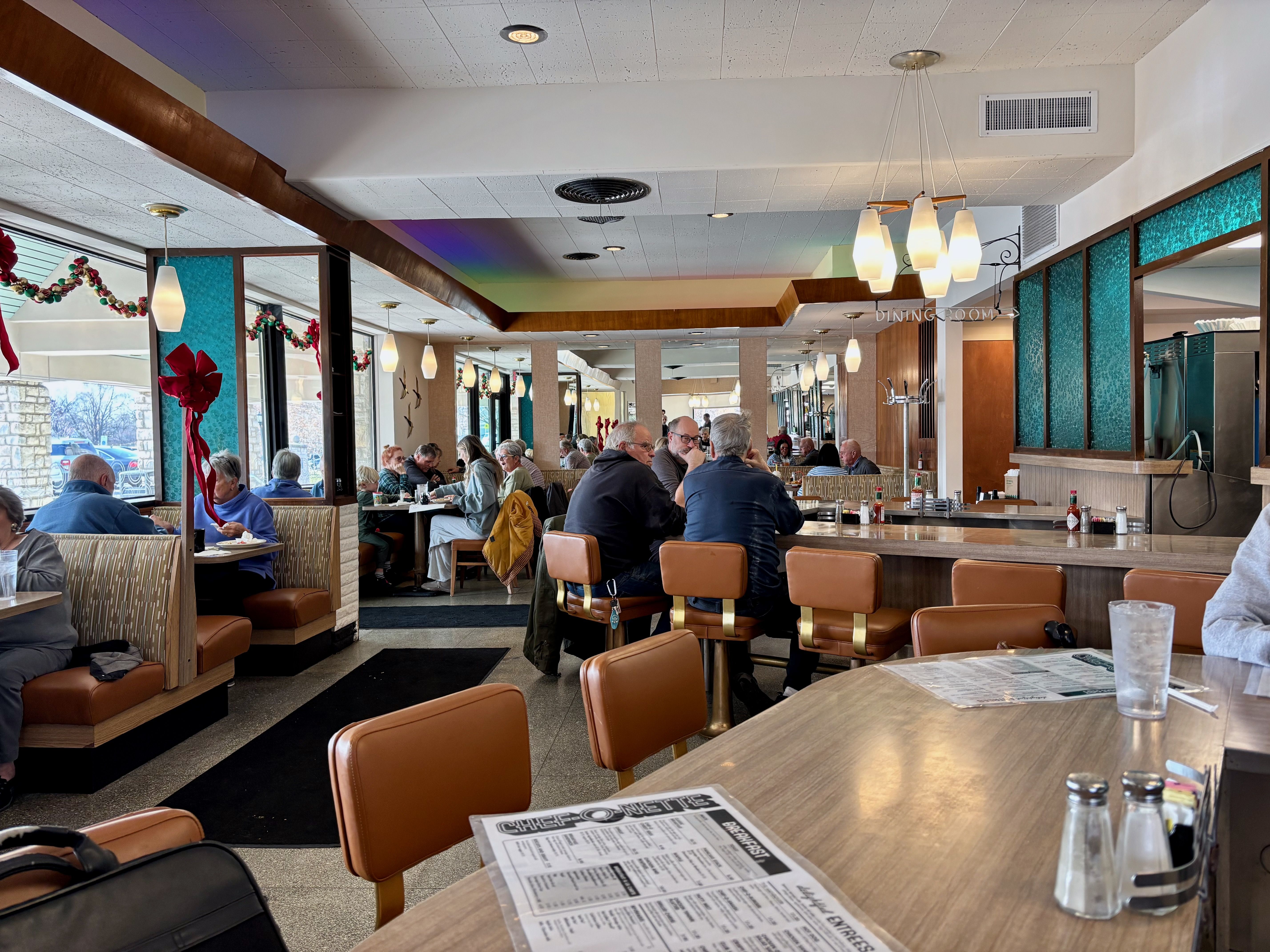 The interior of Chef-O-Nette diner, with blue glass panes, tan swivel bar stools, red Christmas bow decor and several diners.