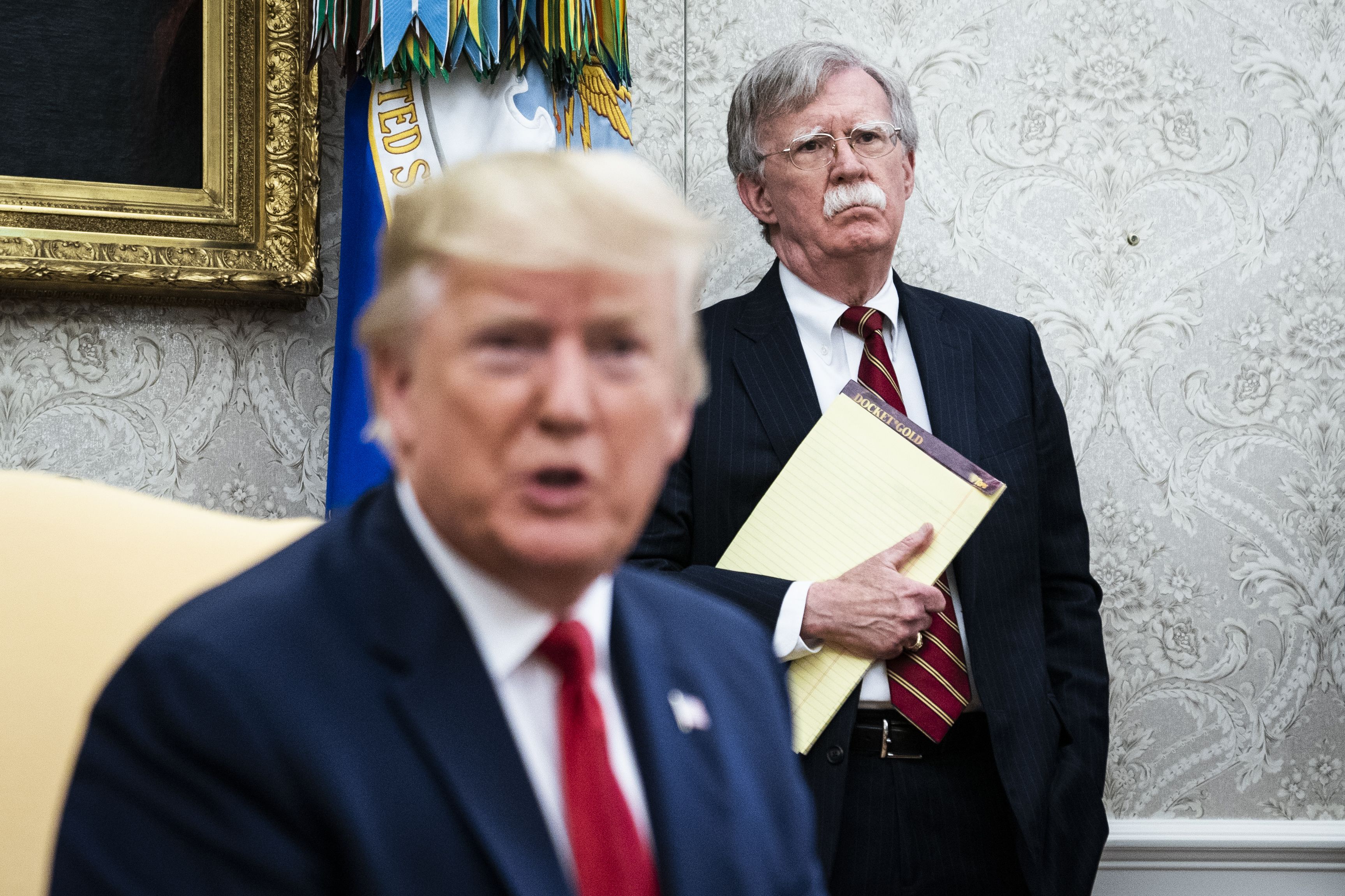 Trump in the foreground, Bolton in the background holding a yellow legal pad