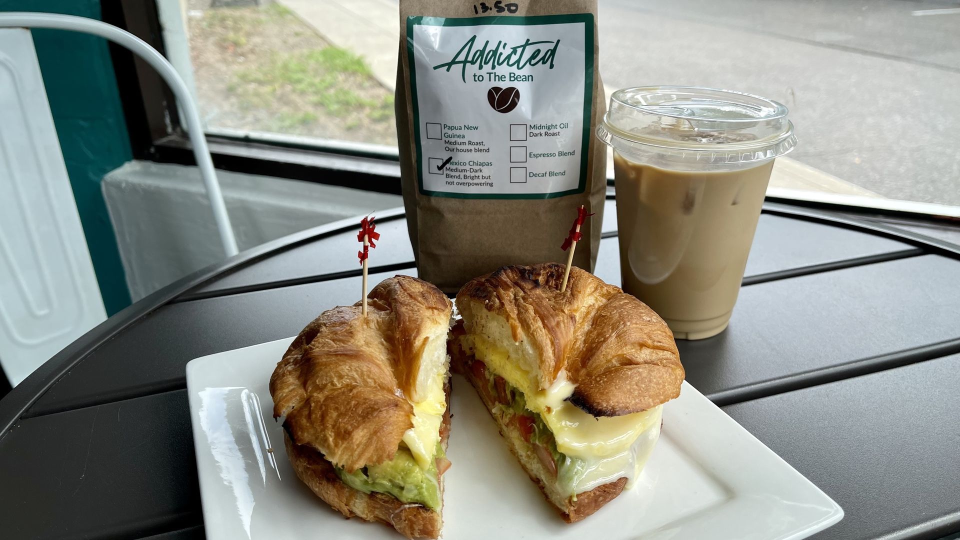 A breakfast sandwich, bag of coffee and iced latte