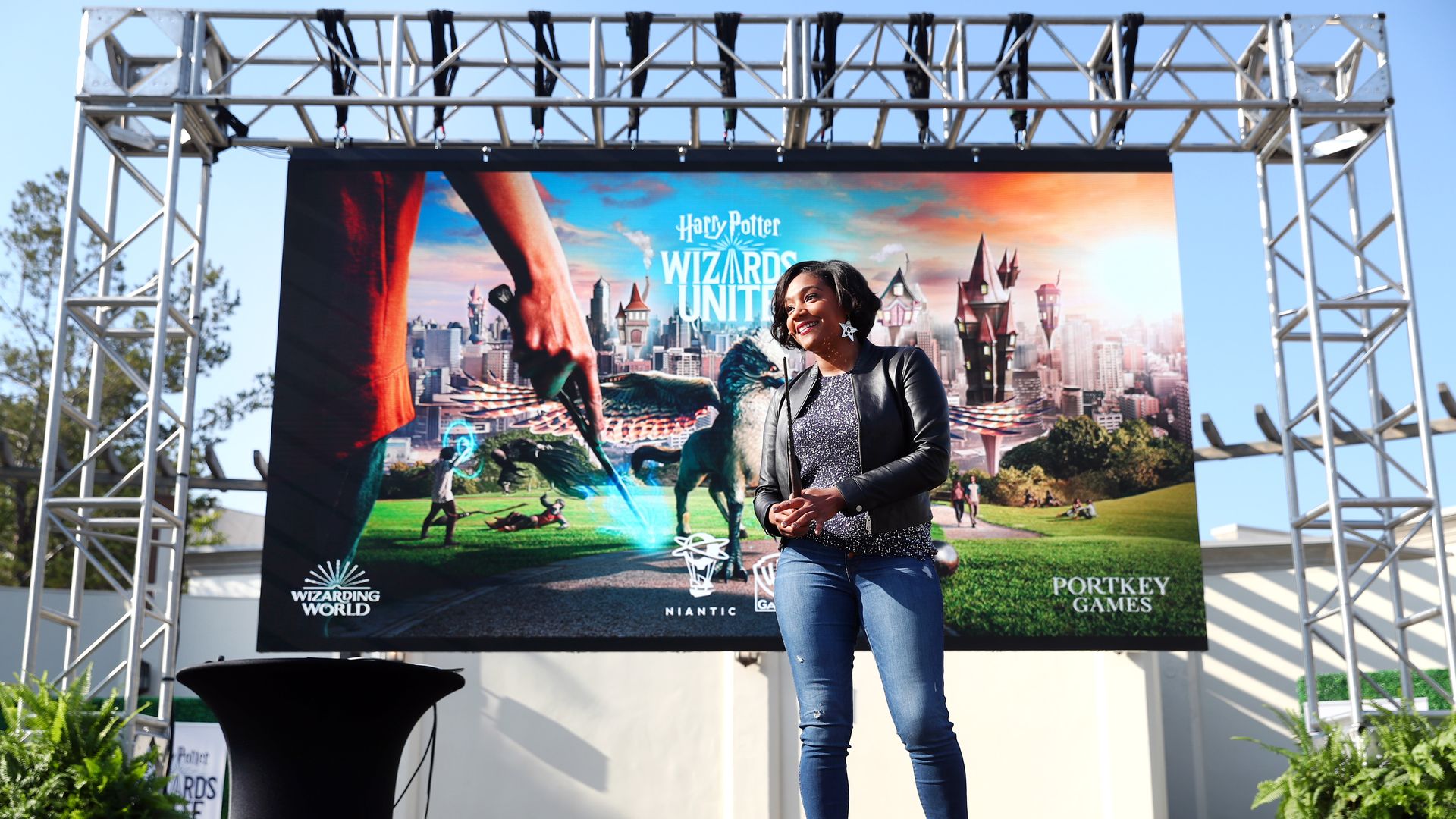 In this image, Tiffany Haddish stands outside on stage with the poster for Wizards Unite behind her.