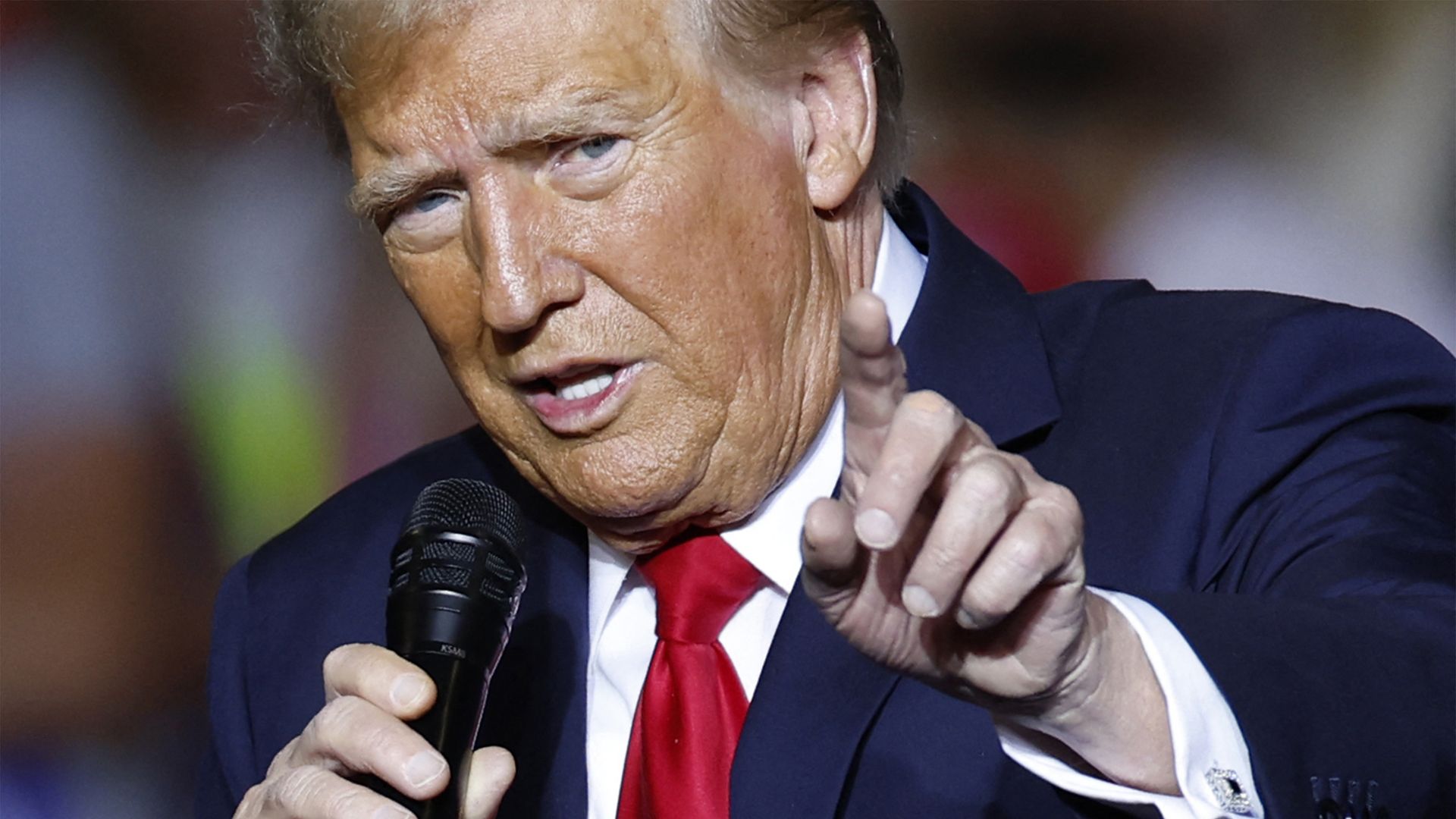 Donald Trump speaks into a microphone and points with his left hand.