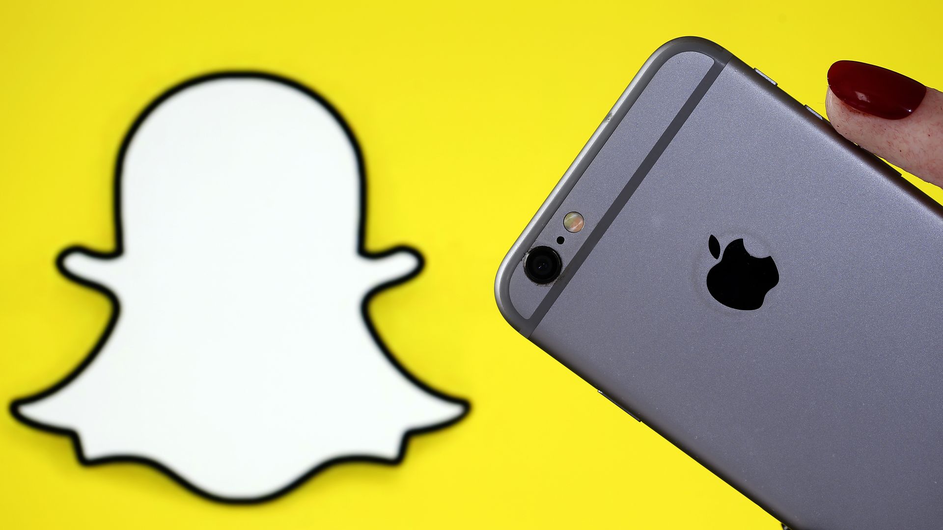 This image is the Snapchat logo and an iphone being held near it.