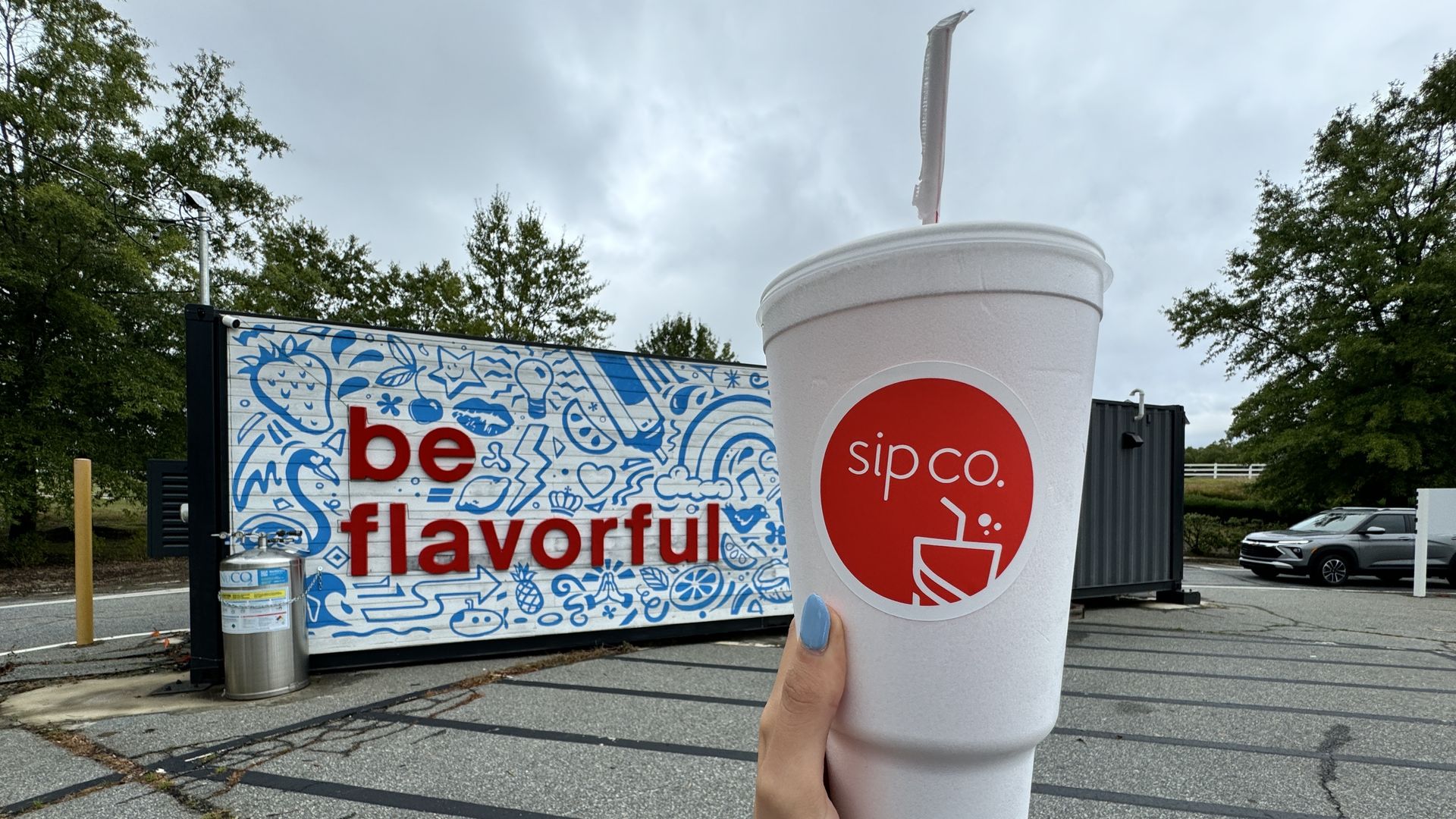 hand holding Styrofoam cup in front of a mural that reads 