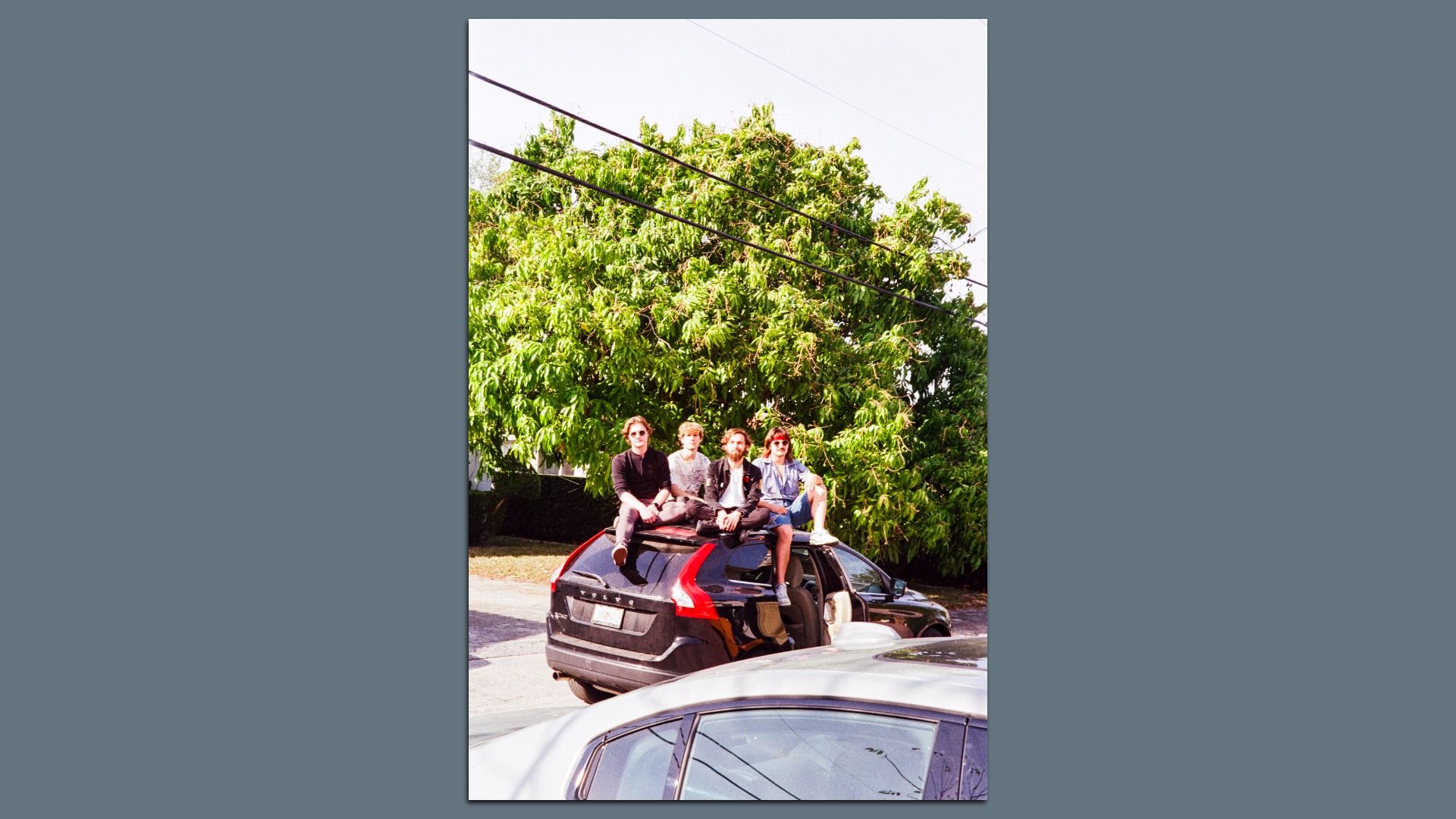 Four guys sitting on a car. 