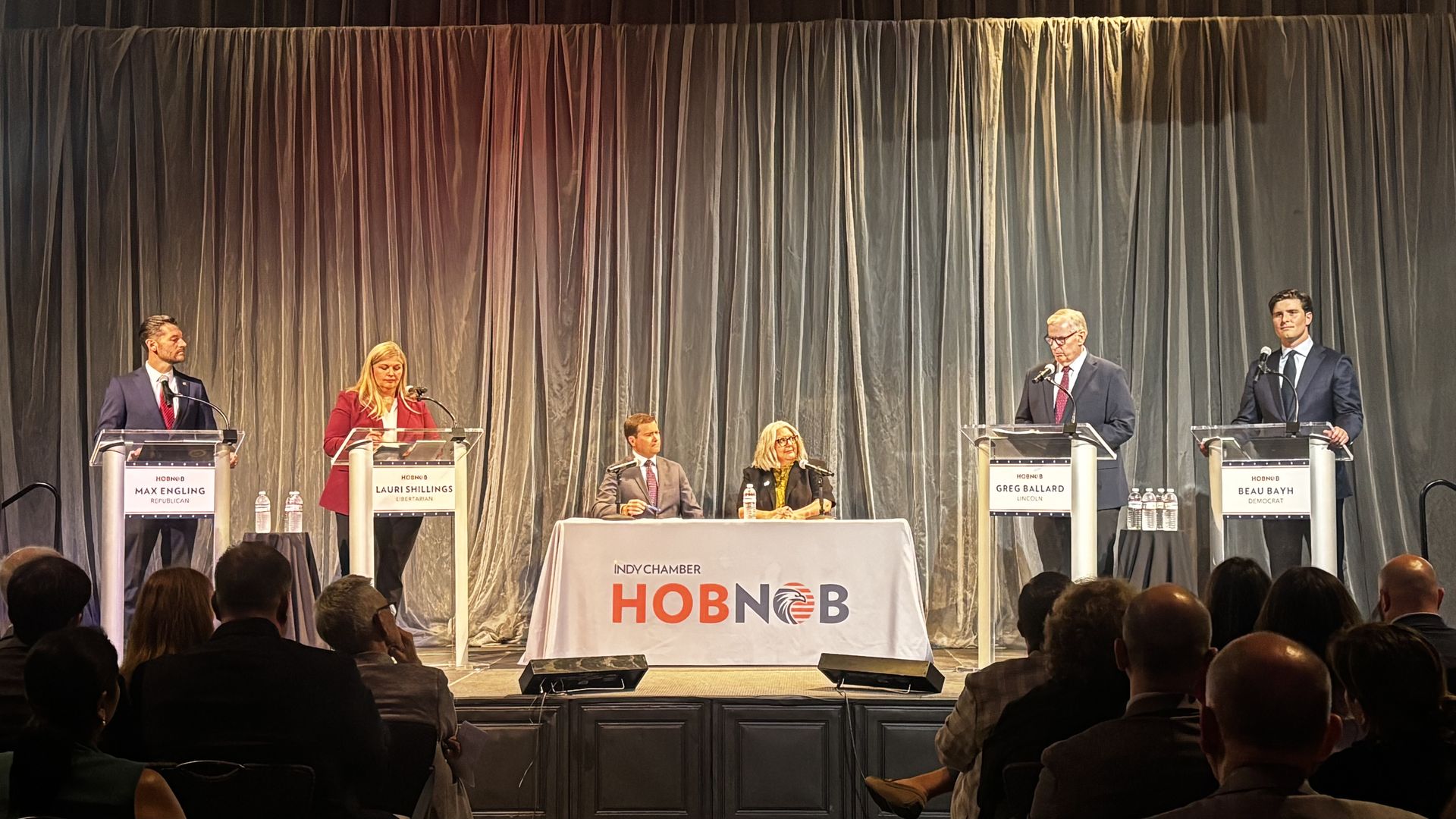 Four people in front of podiums on a stage.