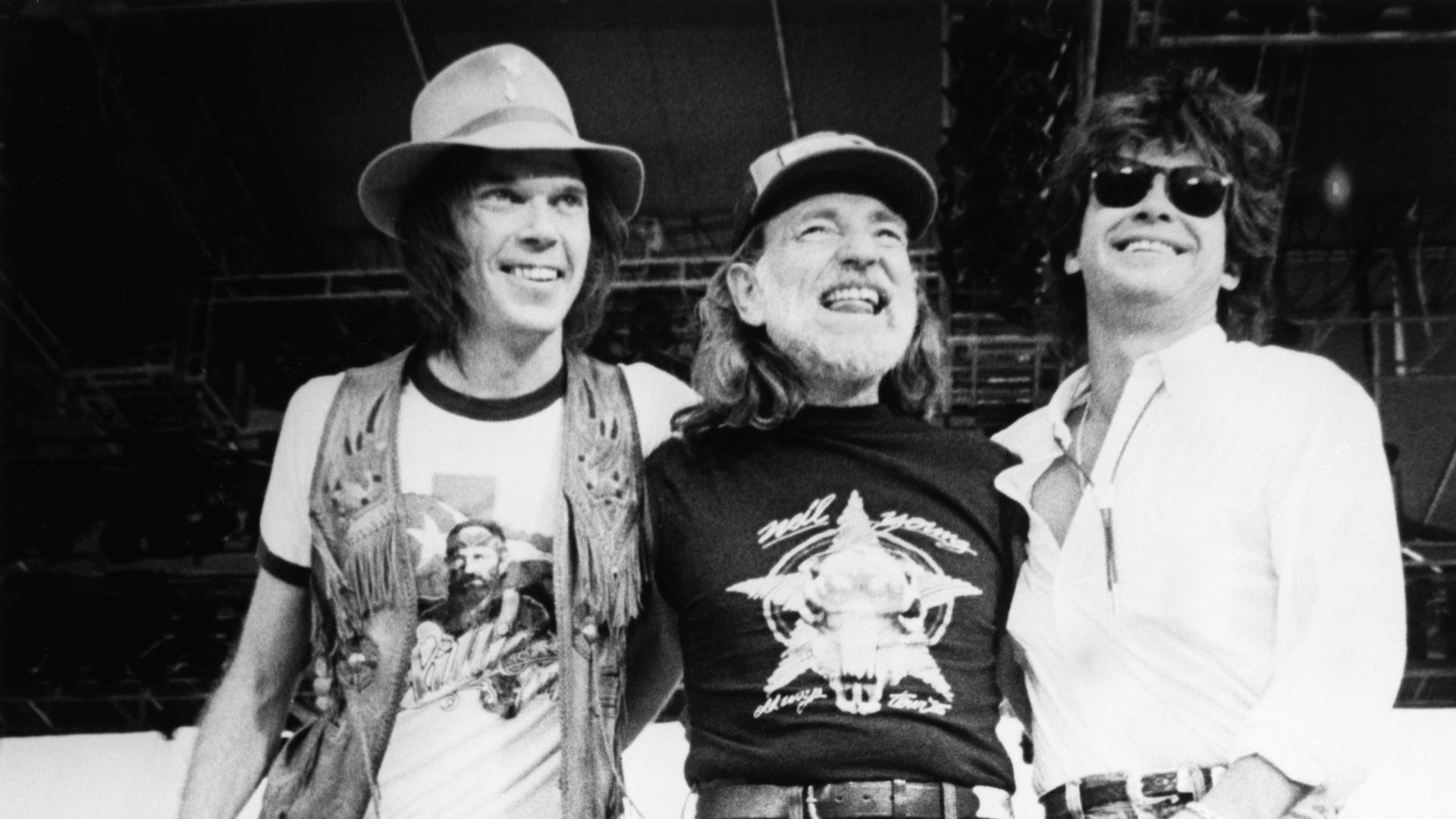 Singer-songwriters Neil Young, Willie Nelson, and John Mellencamp stand together on stage during the 1985 Farm Aid
