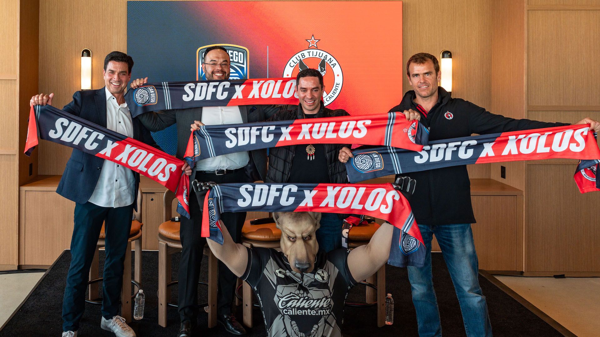Soccer club owners and a dog mascot hold up scarves.