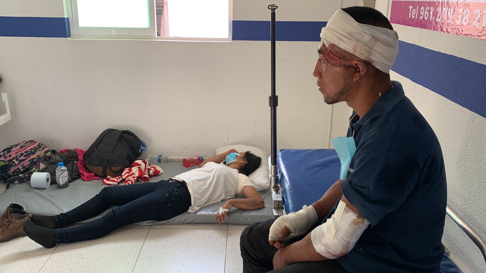 a man who is injured and bandaged sits while another woman lays down