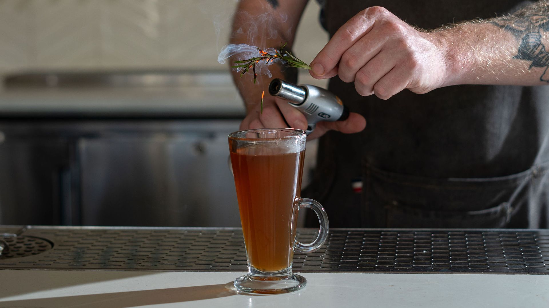 A bartender ignites rosemary over a cider cocktail