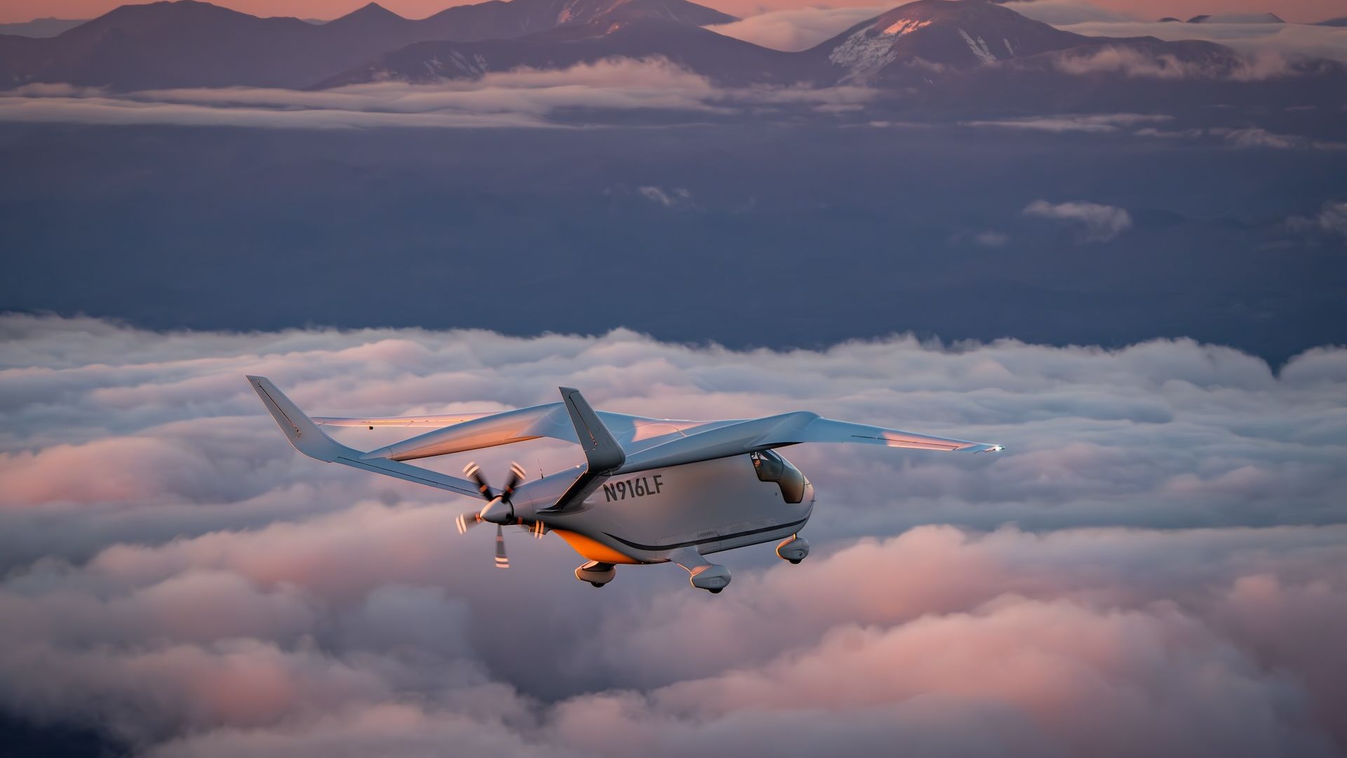 Photo of a Beta technologies aircraft flying above clouds with mountains in the background. 