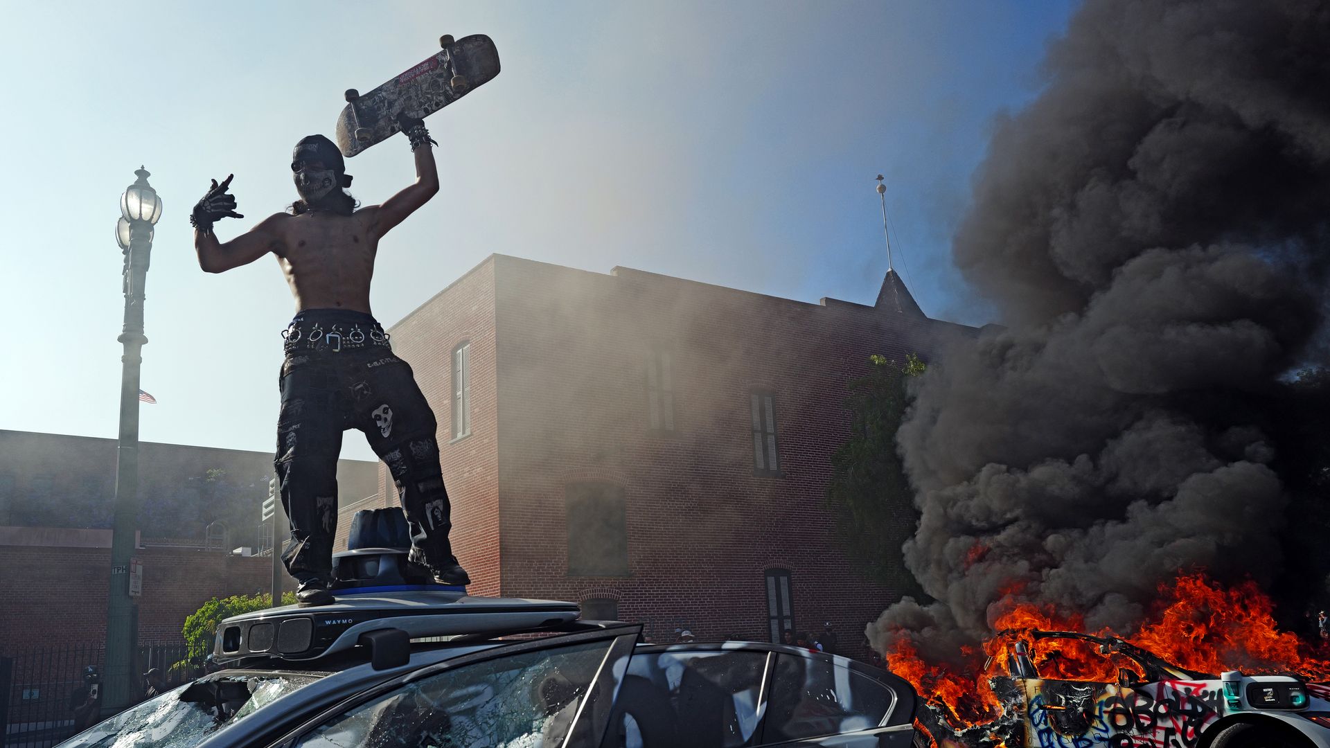 A protestor stands on a vandalized Waymo car during a protest against immigration raids on June 08, 2025 in Los Angeles, California. Tensions in the city remain high after the Trump administration called in the National Guard against the wishes of city leaders following two days of clashes with poli