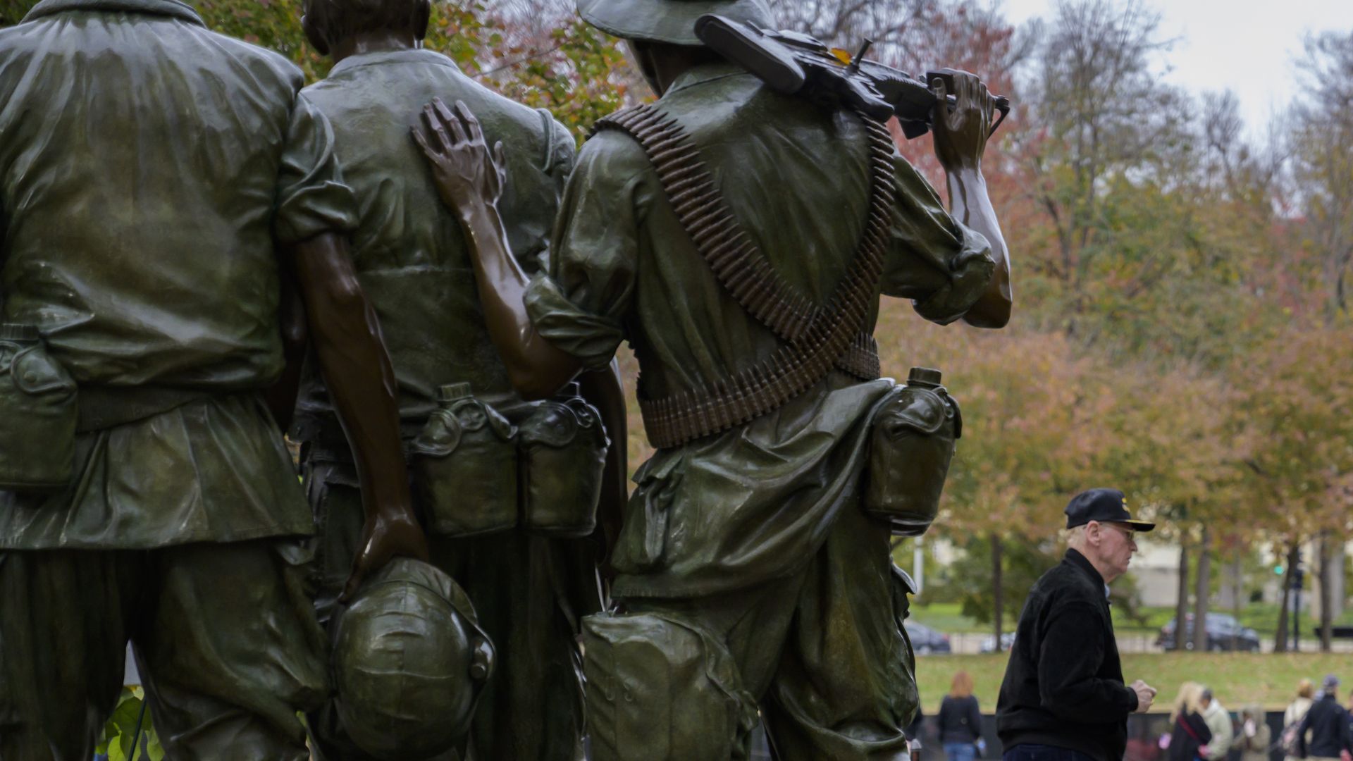 In this image, a Vietnam veteran walks past a large green statue of three soldiers in a park. 